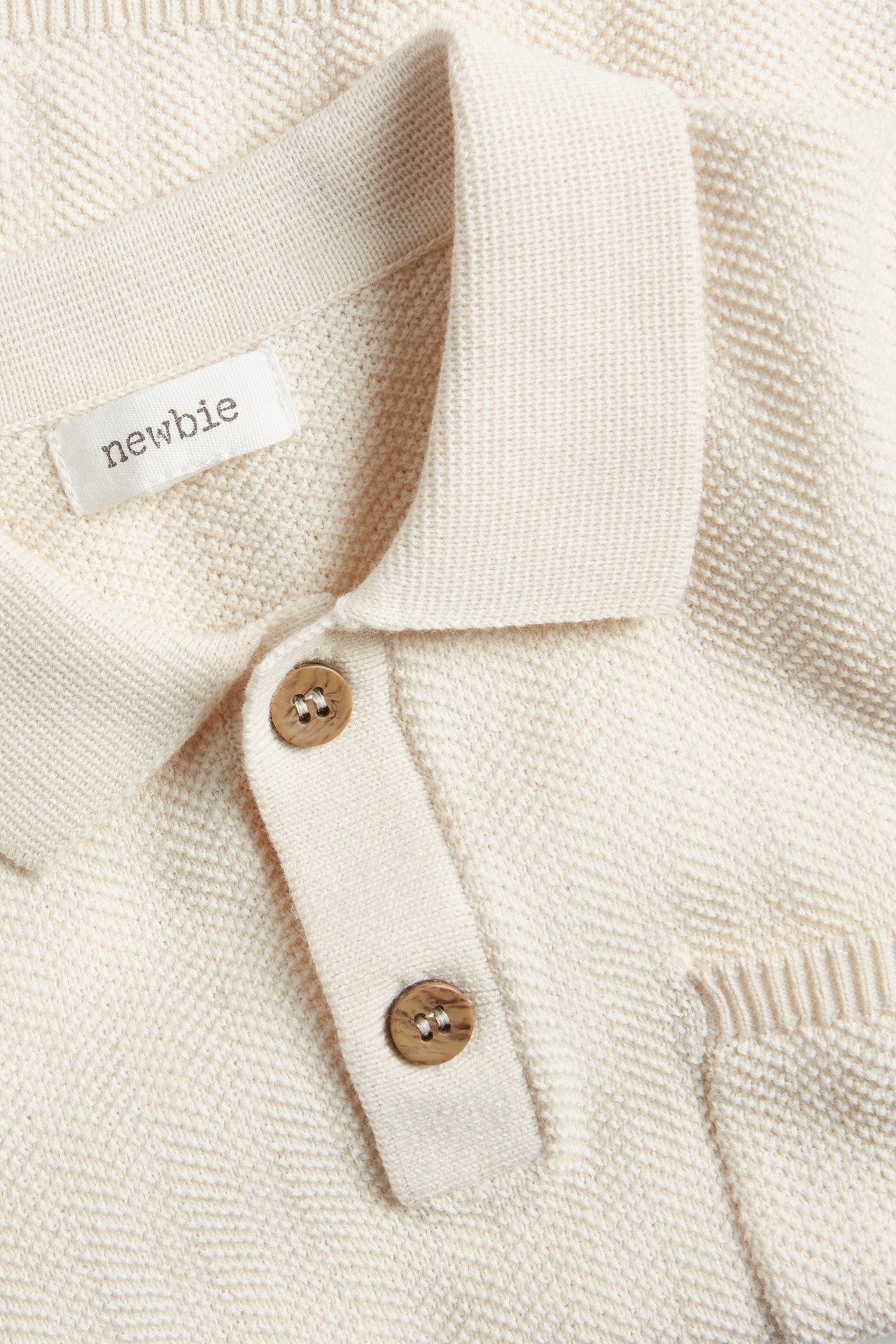 Nahaufnahme eines hellbeigen gestrickten Baumwoll-Poloshirts mit Kragen und zwei braunen Knöpfen.