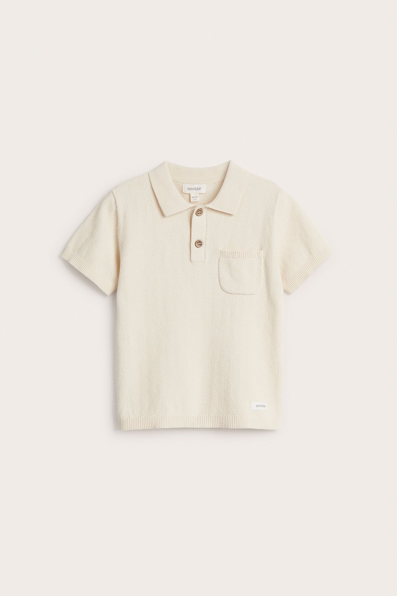 Vorderansicht: Kinder hellbeiges gestricktes Baumwoll-Poloshirt mit Kragen, zwei Knöpfen und Brusttasche.