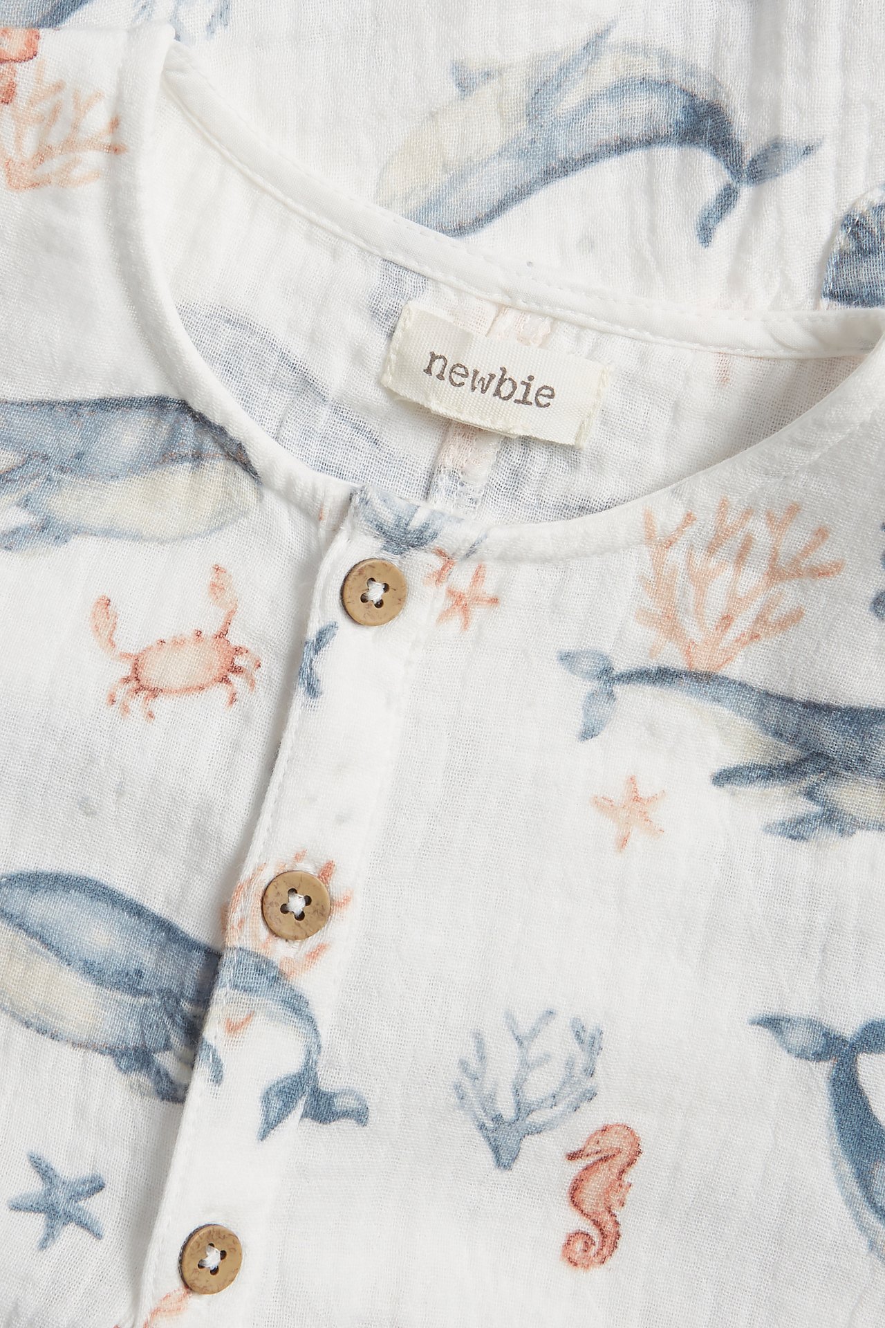 Close-up of a baby's off-white cotton muslin playsuit with blue sea animal pattern and front buttons.