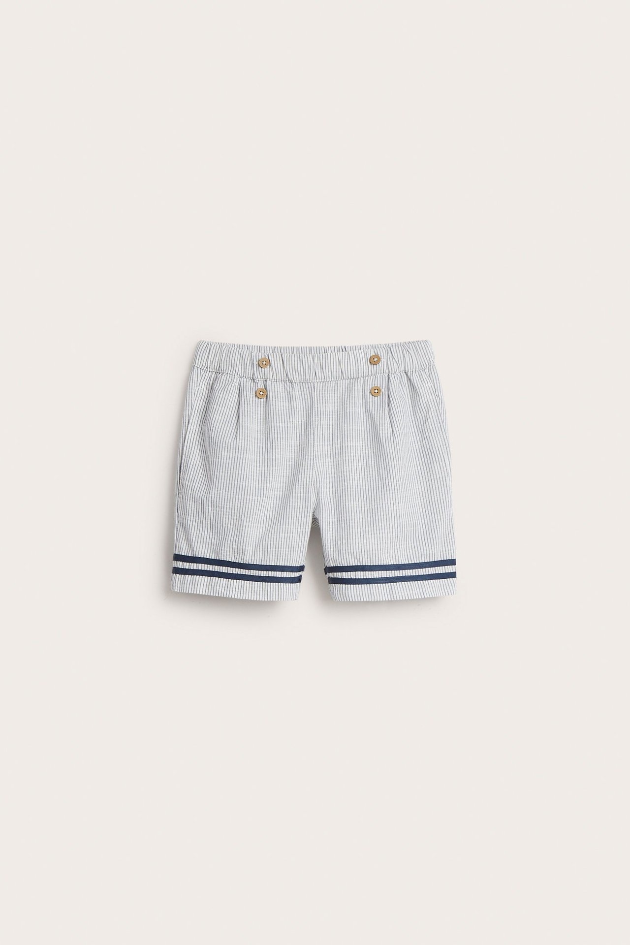 Vorderansicht: gestreifte Kinder-Baumwollshorts in Off-White mit Gummibund, Zierknöpfen und blauen Streifen.