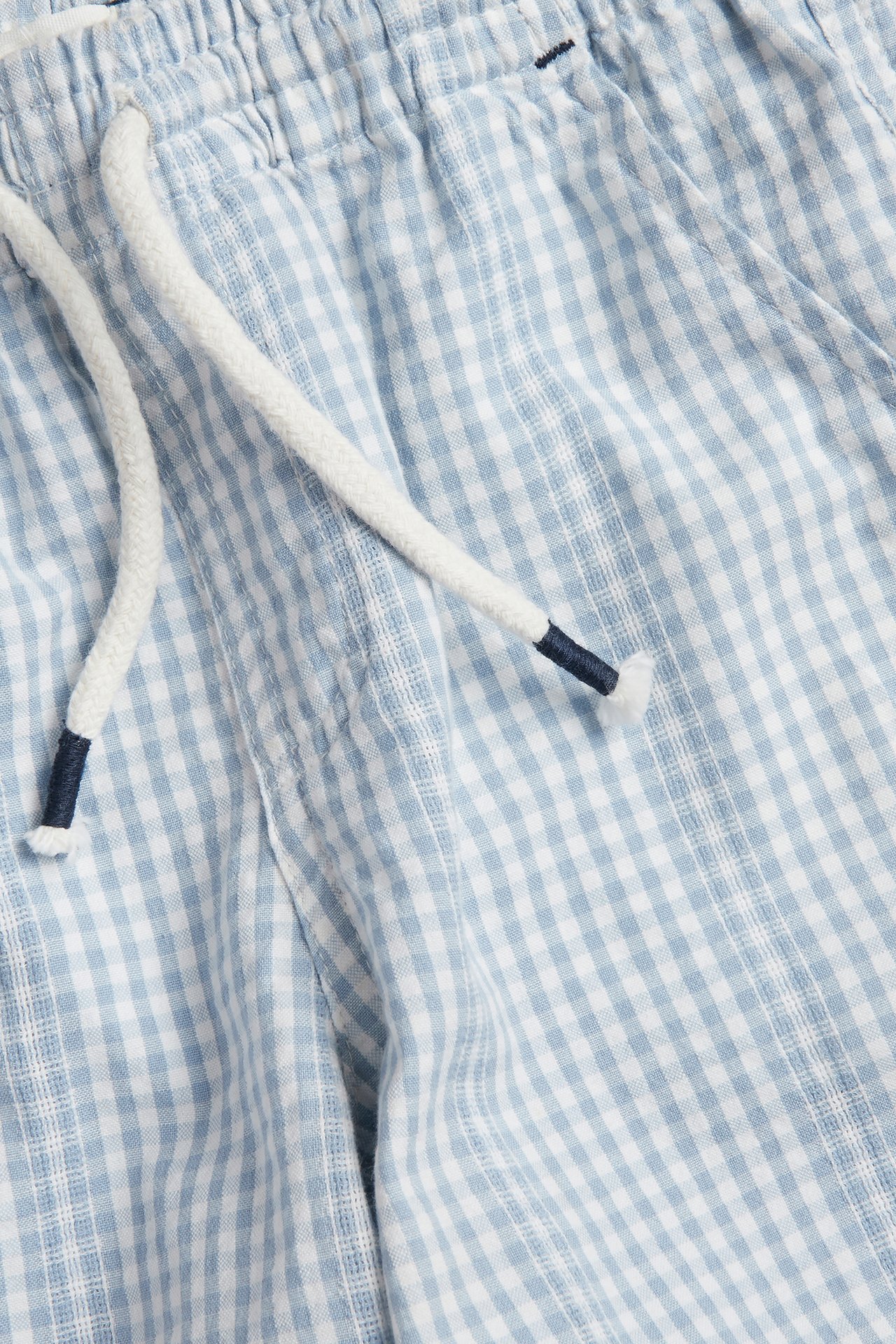 Close-up of light blue and off-white checked cotton shorts with an elastic waistband and white drawstring.