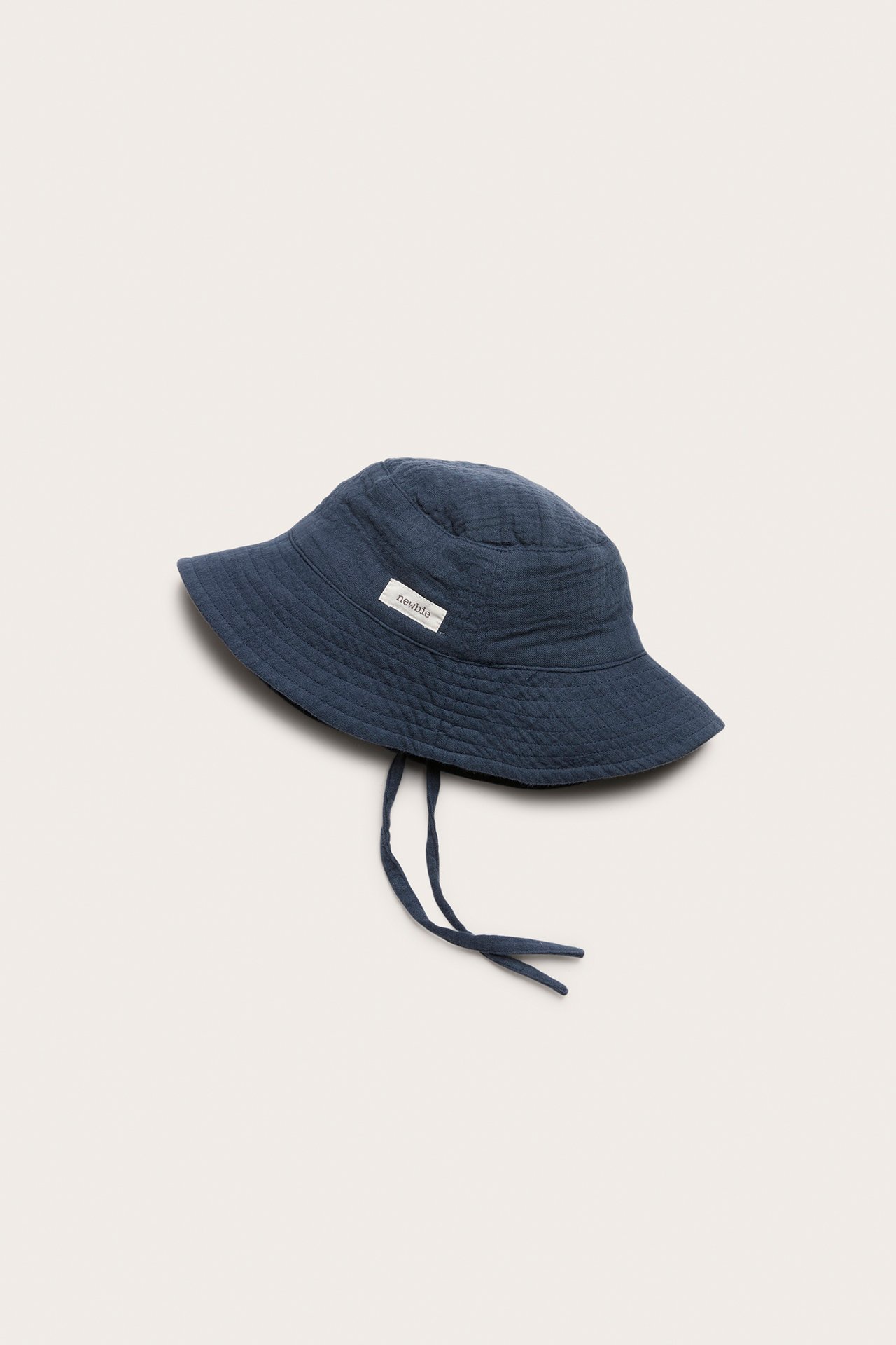 Side view of a dark blue woven baby/kid's bucket hat with tie straps.