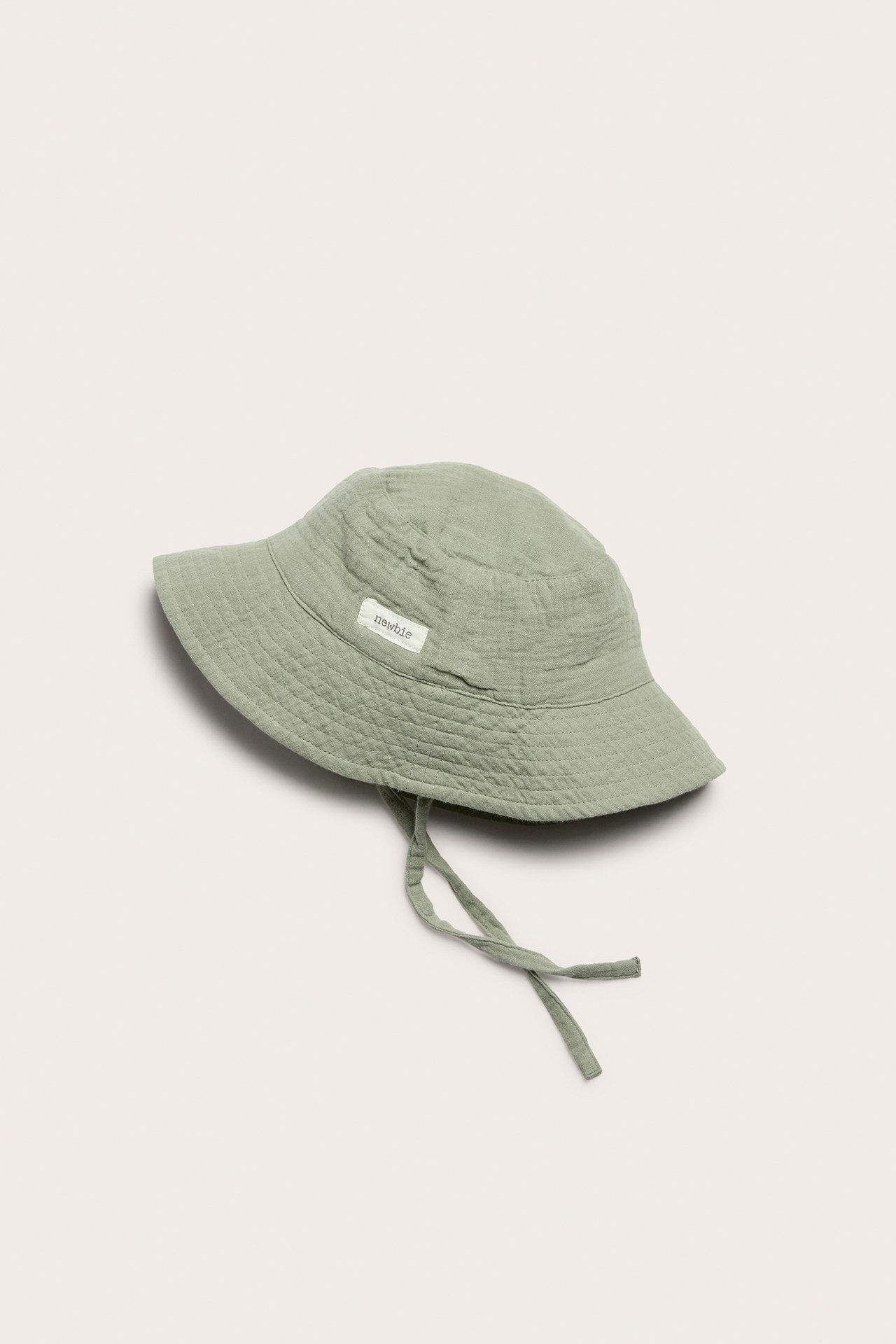 Side view of a green woven baby bucket hat with tie straps and a soft brim.
