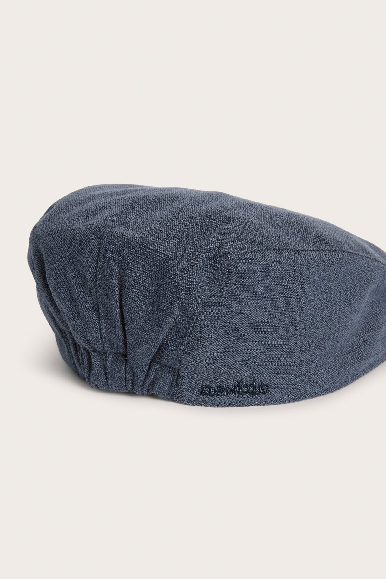 Close-up side view of a dark blue structured baby/kid's flat cap with elastic back and embroidery.