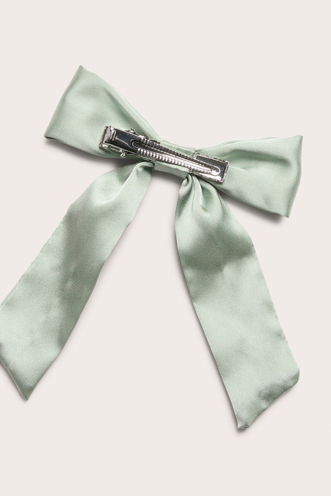 Close-up, top view of a light green satin bow hair clip with a silver metal fastening.