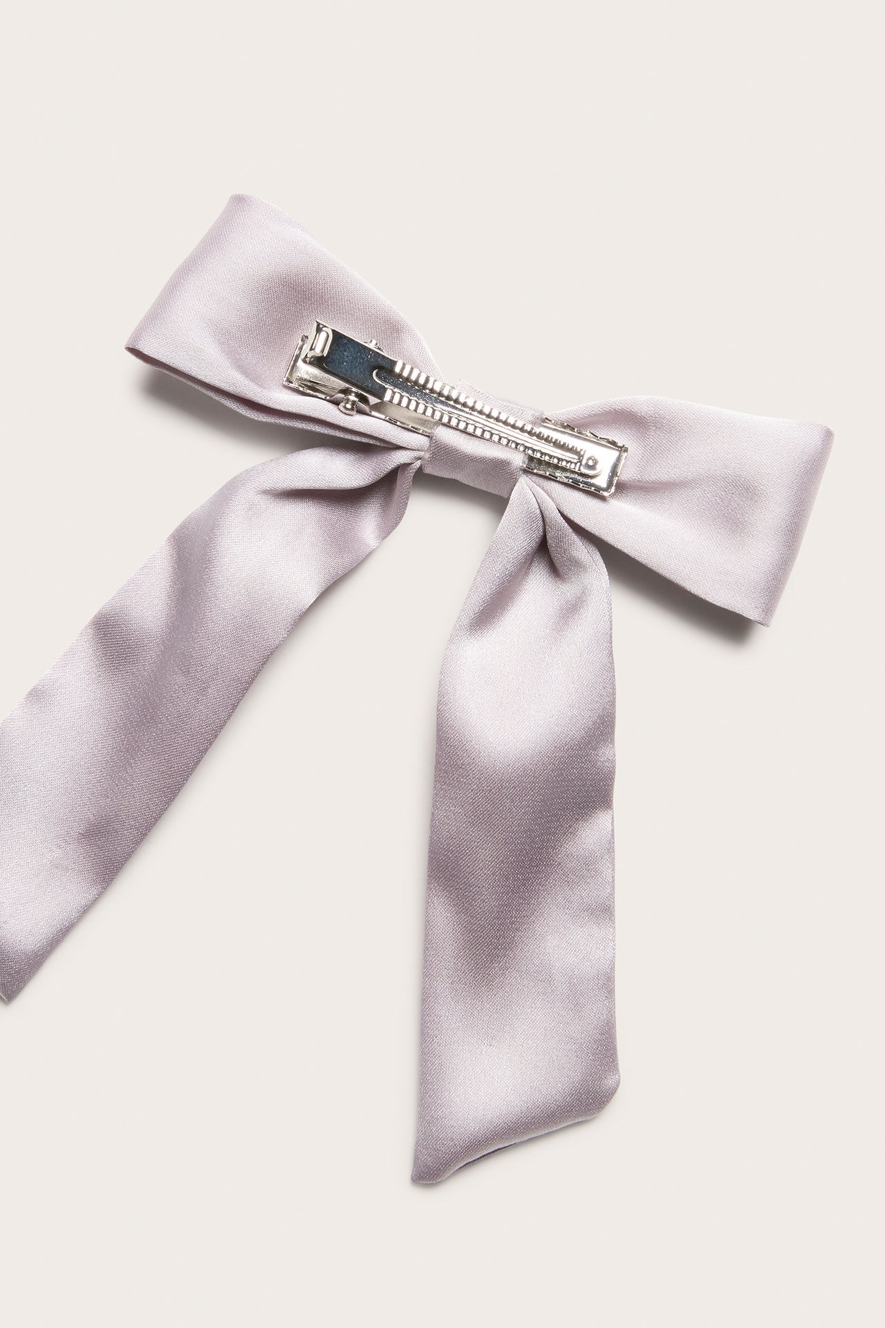 Close-up, top view of a light lilac satin bow hair clip with a silver metal fastener.