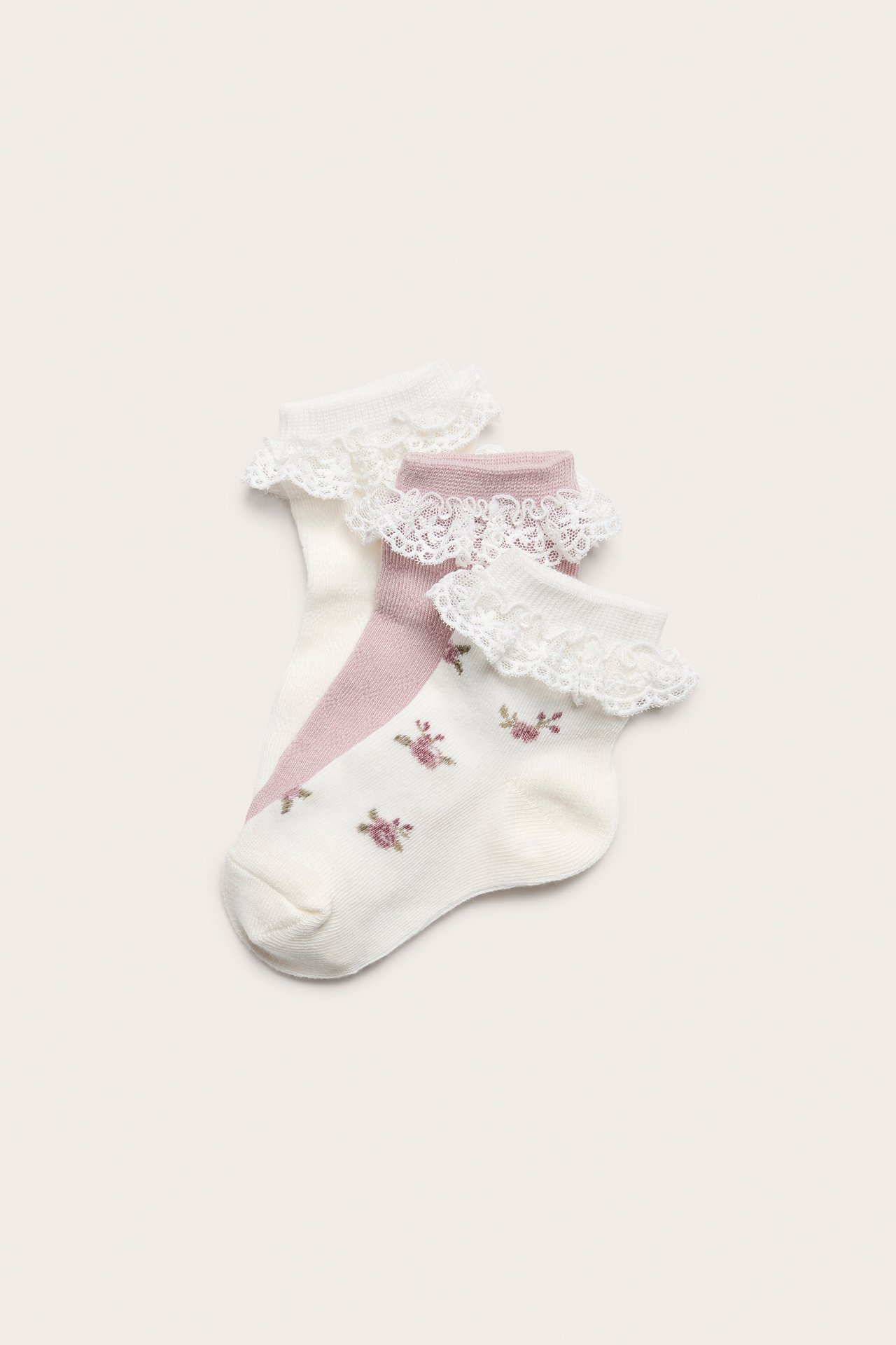 Front view of baby socks: off-white floral, off-white pointelle, and light pink pointelle, with white lace ruffles.
