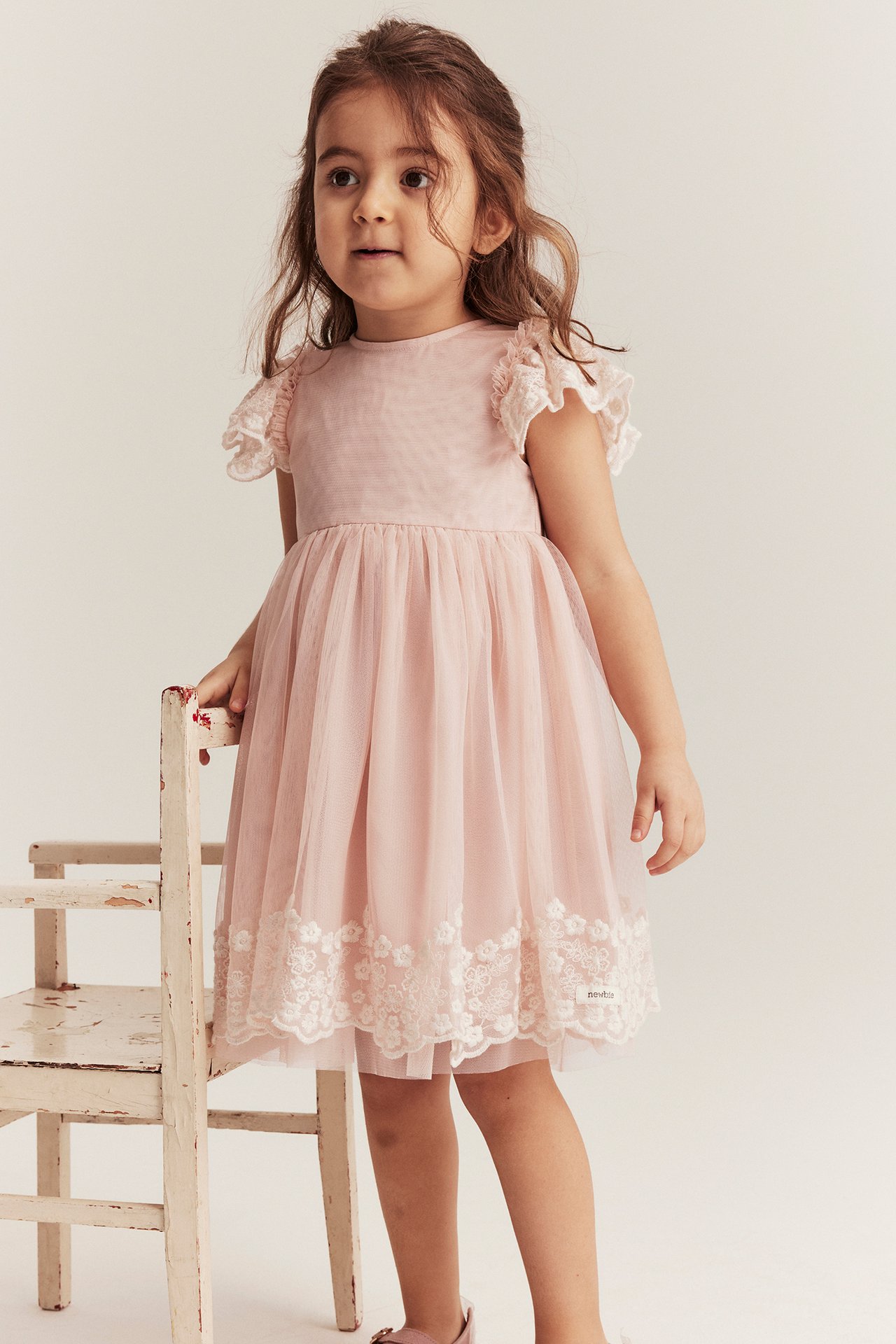 Vorderansicht: Kind in hellrosa Netz-Kleid mit Rüschenärmeln und weißer Blumenstickerei.