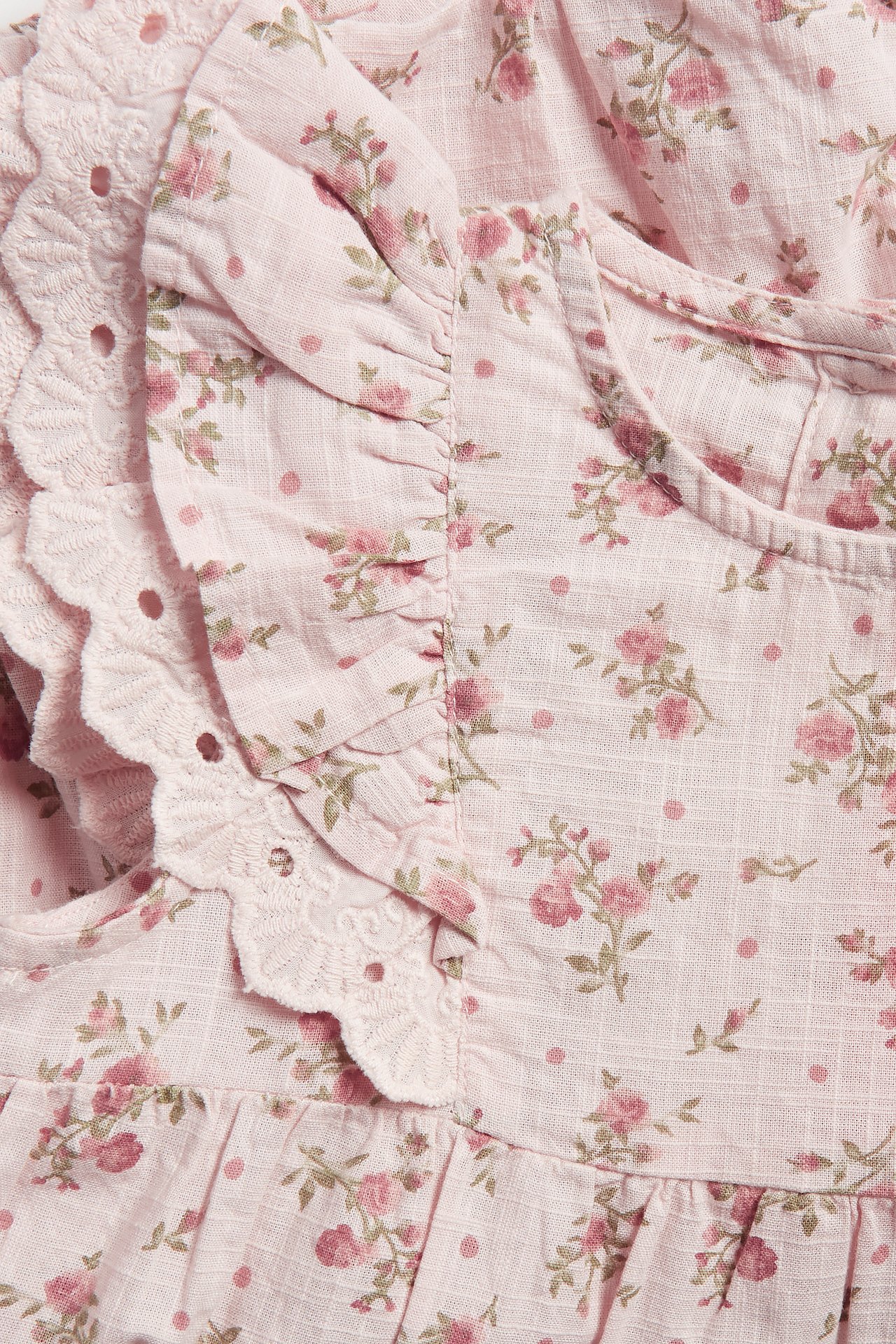 Close-up of a light pink baby playsuit with a small floral pattern and ruffle sleeves with lace trim.