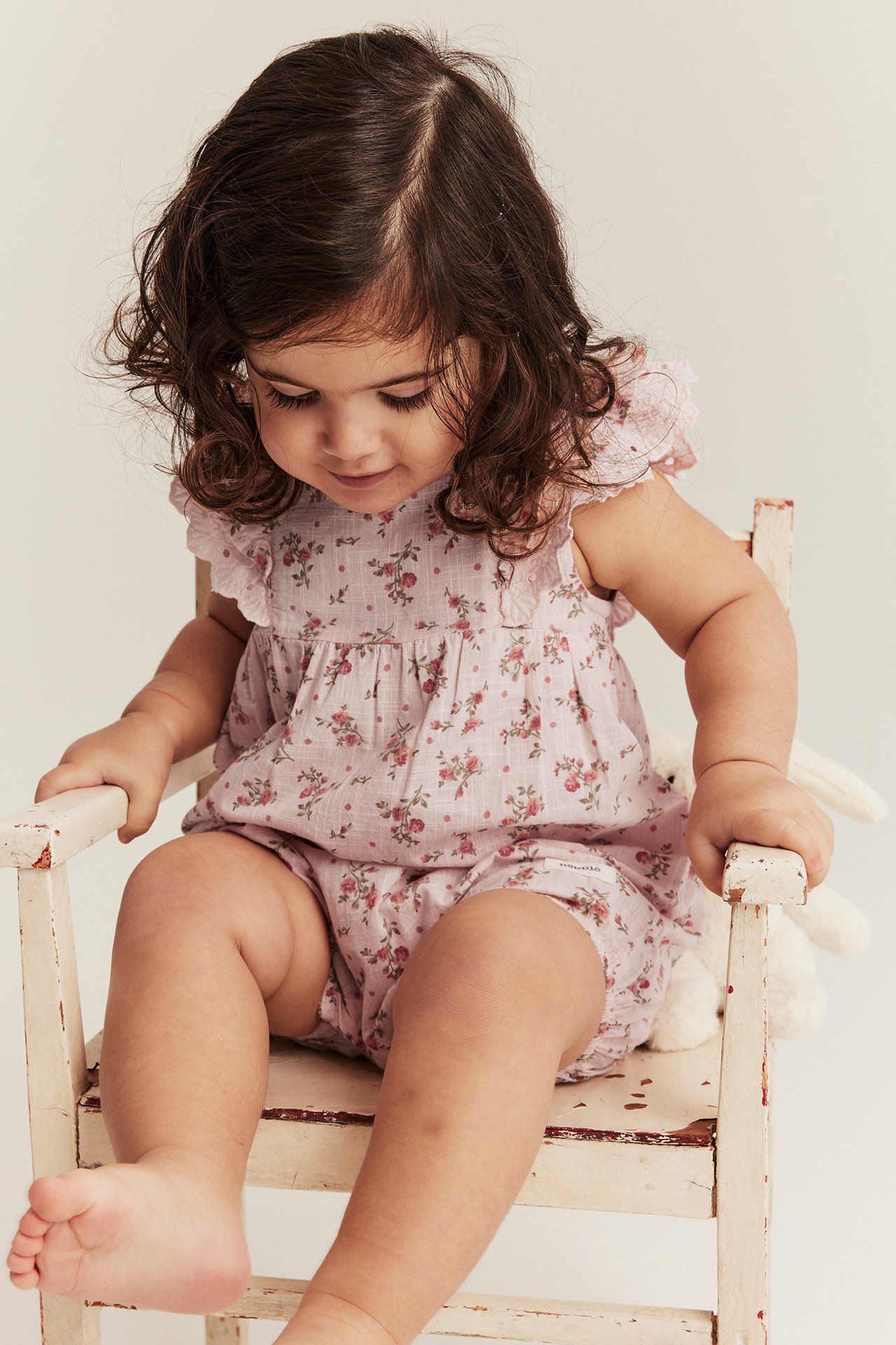 Front view of a baby wearing a light pink floral cotton playsuit with ruffle lace sleeves.