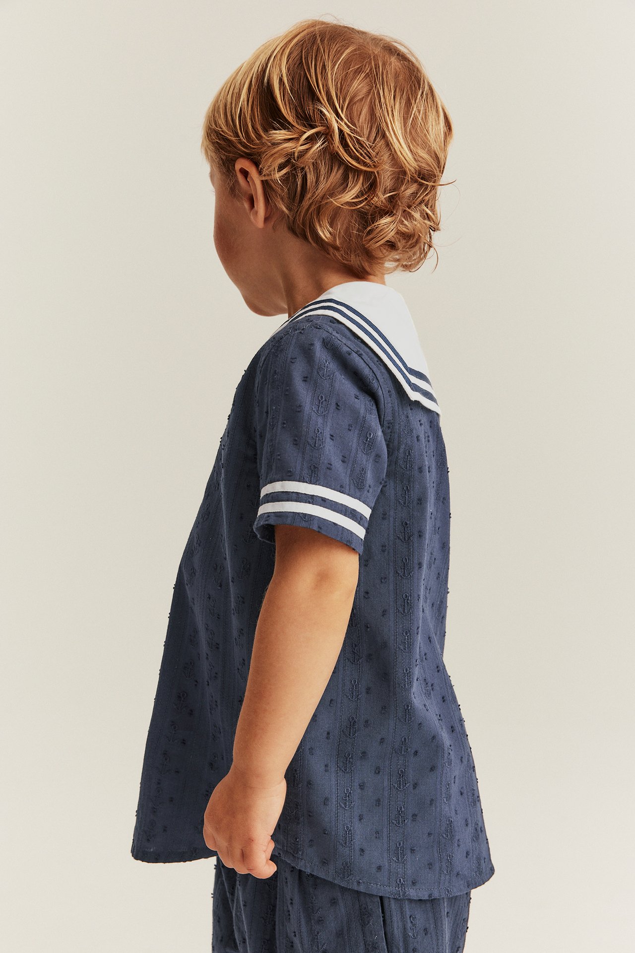 Side view of a kid in a dark blue textured shirt with white sailor collar and matching shorts.