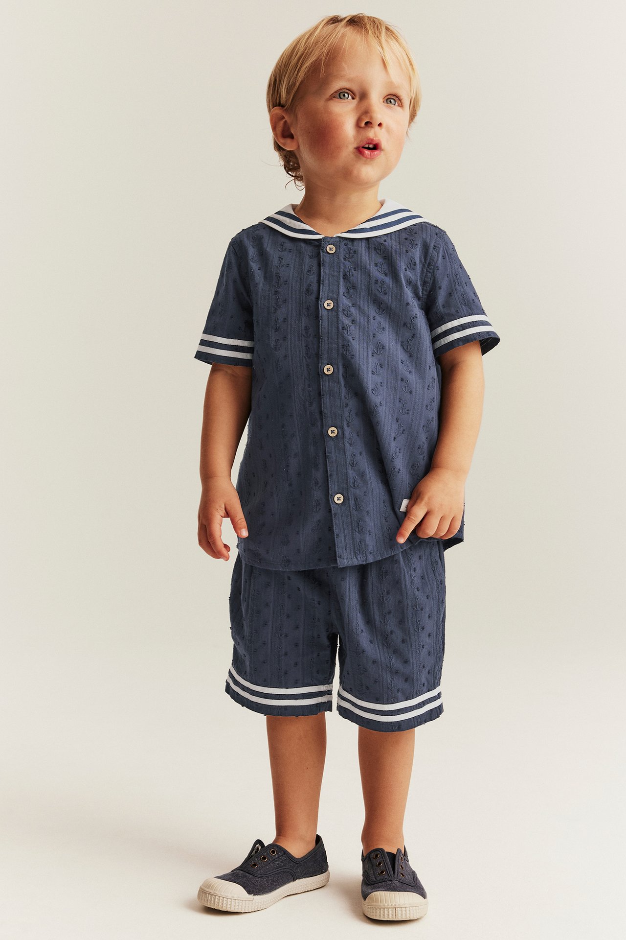 Front view of a kid in a dark blue textured short-sleeved sailor shirt, matching shorts, and shoes.