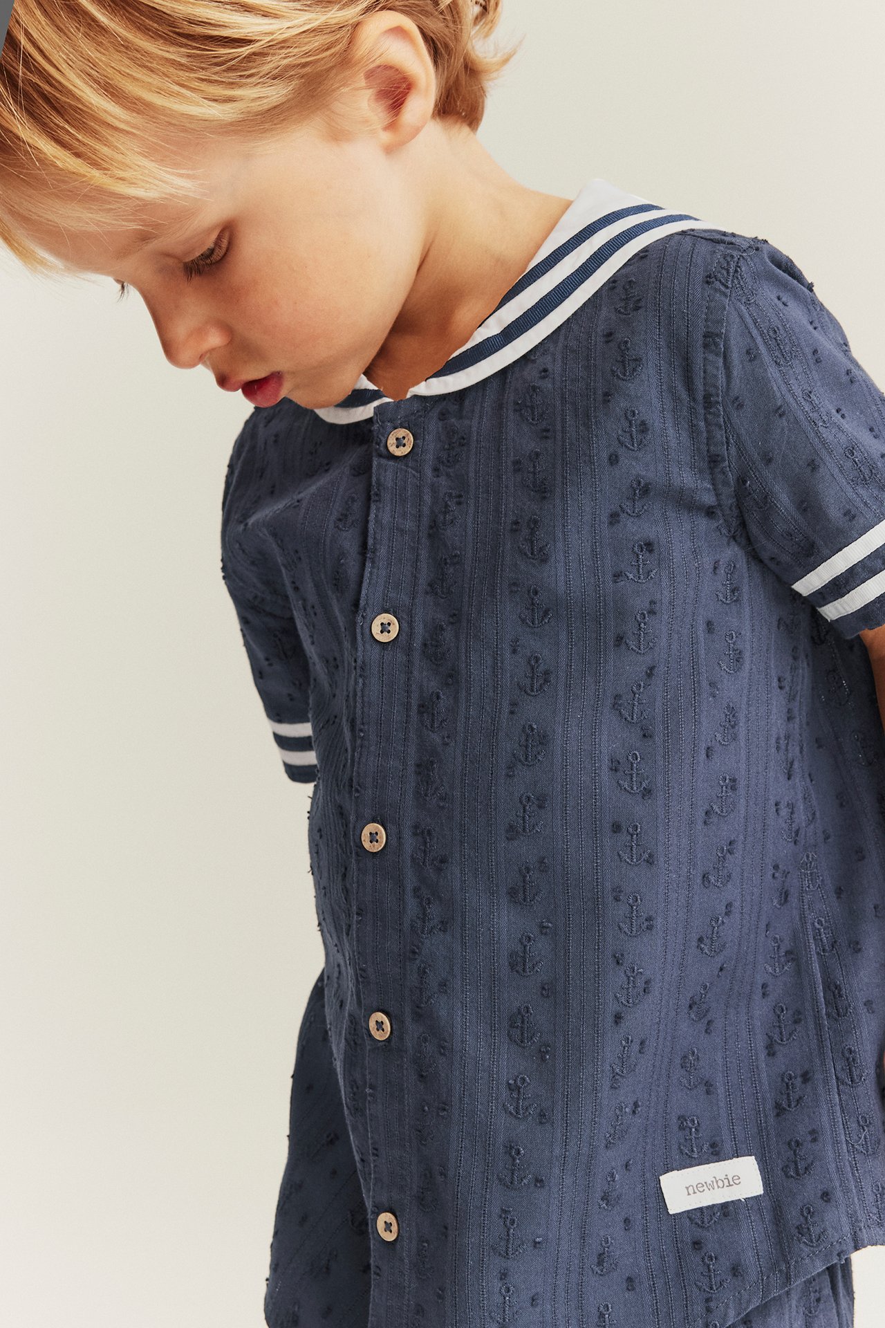 Close-up: Kid in dark blue short-sleeved cotton shirt with sailor collar, anchor pattern, and matching shorts.