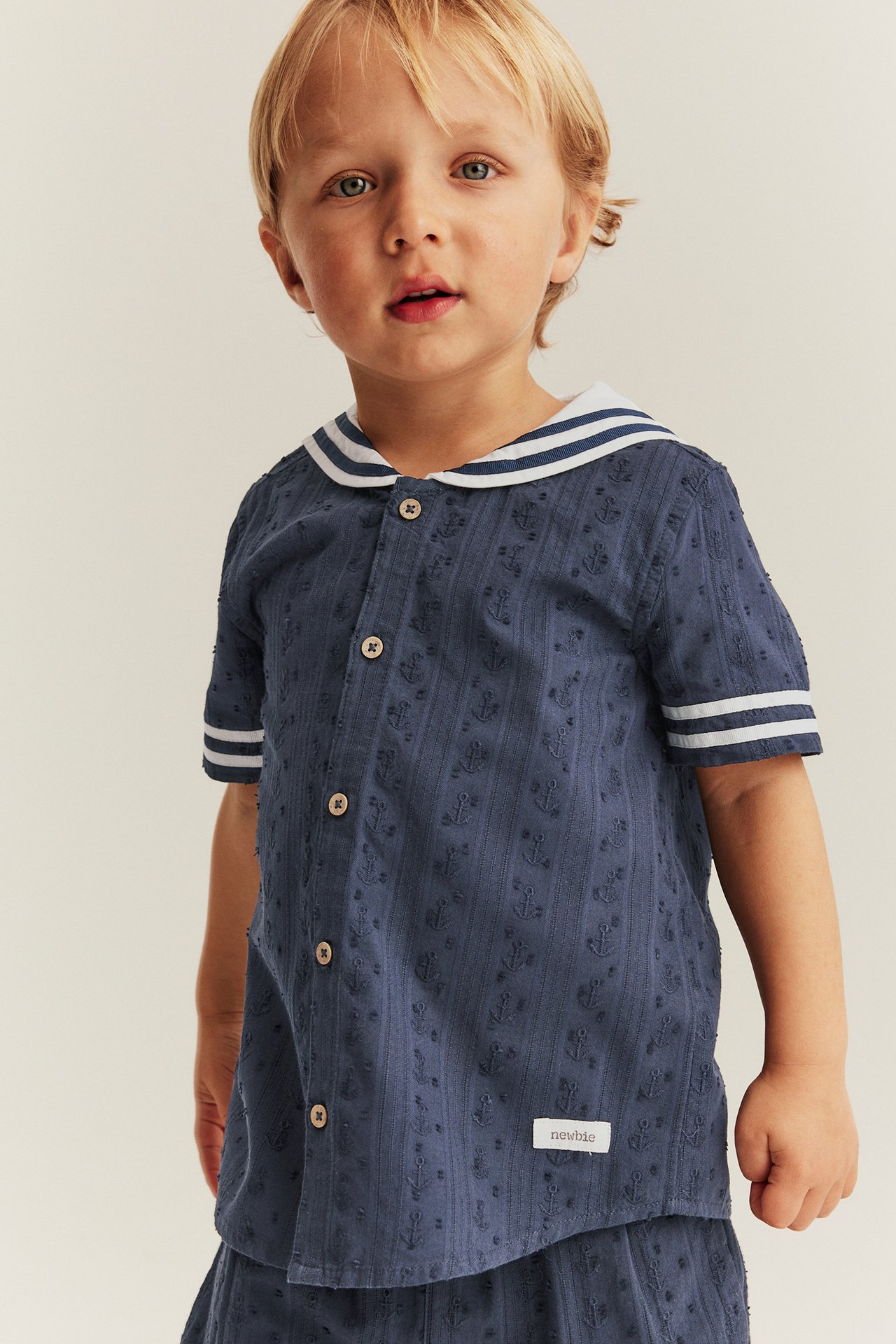 Front view: Kid in dark blue short-sleeved shirt with white-striped sailor collar, anchor pattern, and matching shorts.