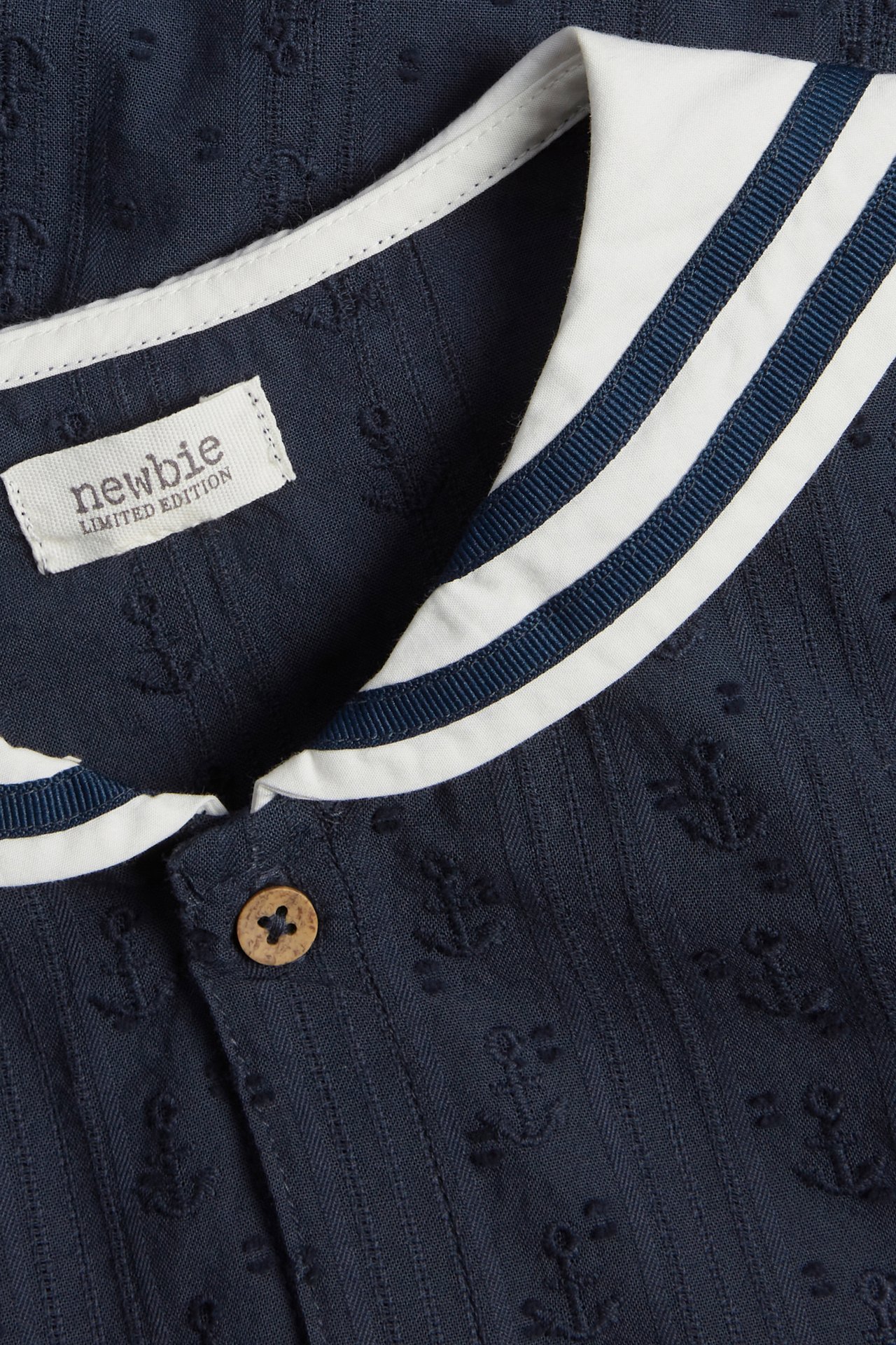 Close-up of a dark blue cotton shirt with a white striped sailor collar, subtle anchor pattern, and wooden button.
