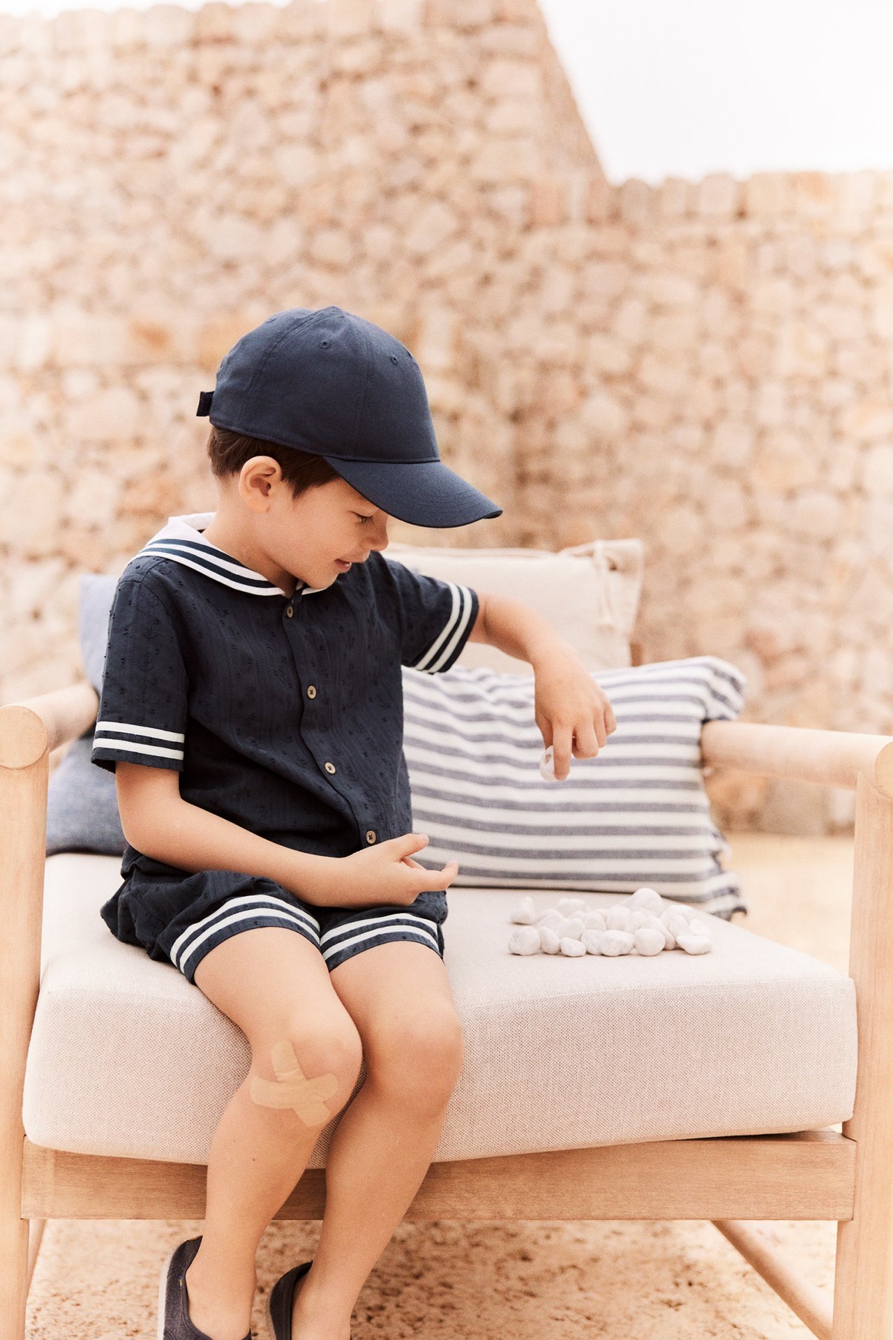 Kid wears a dark blue sailor shirt, matching shorts with white stripes, and a dark blue cap.