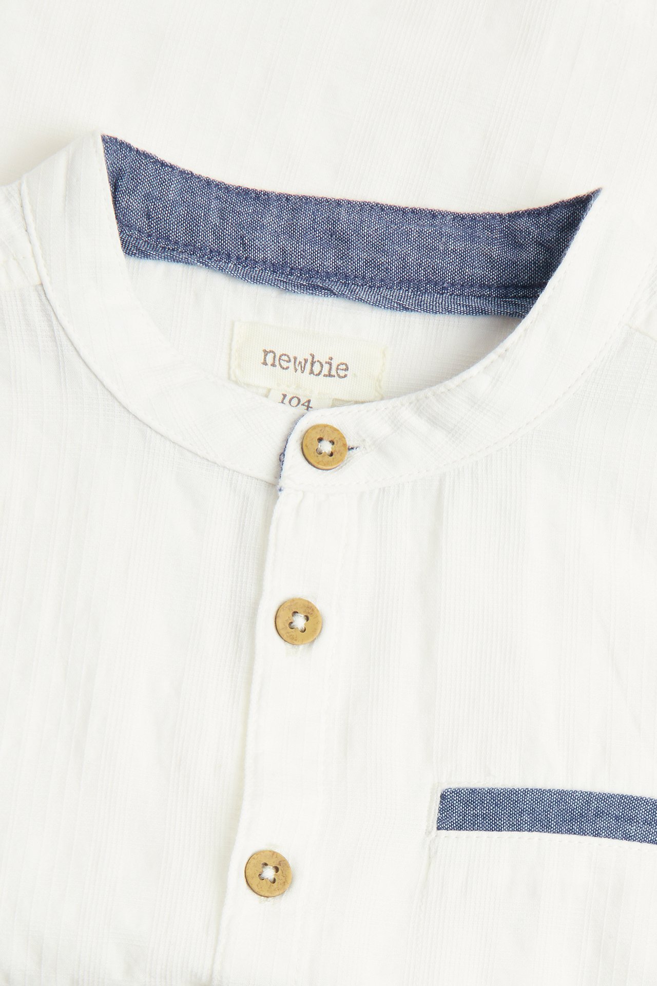 Nahaufnahme: Kinder-Offwhite-Baumwollhemd mit blauem Chambray-Stehkragen, Kokosknöpfen und Tasche.
