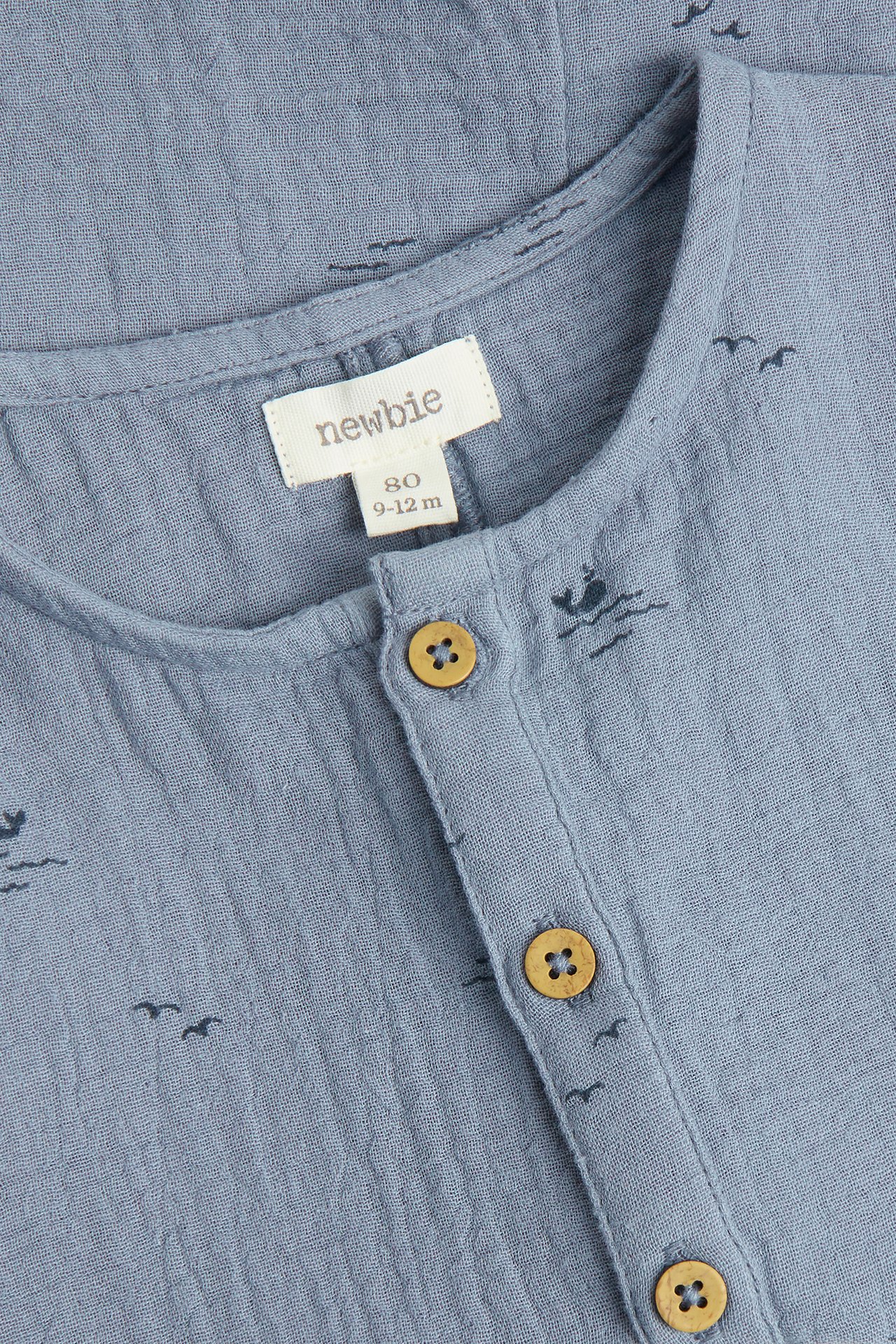Close-up of a baby's blue cotton playsuit with whale and bird patterns, featuring wooden front buttons.