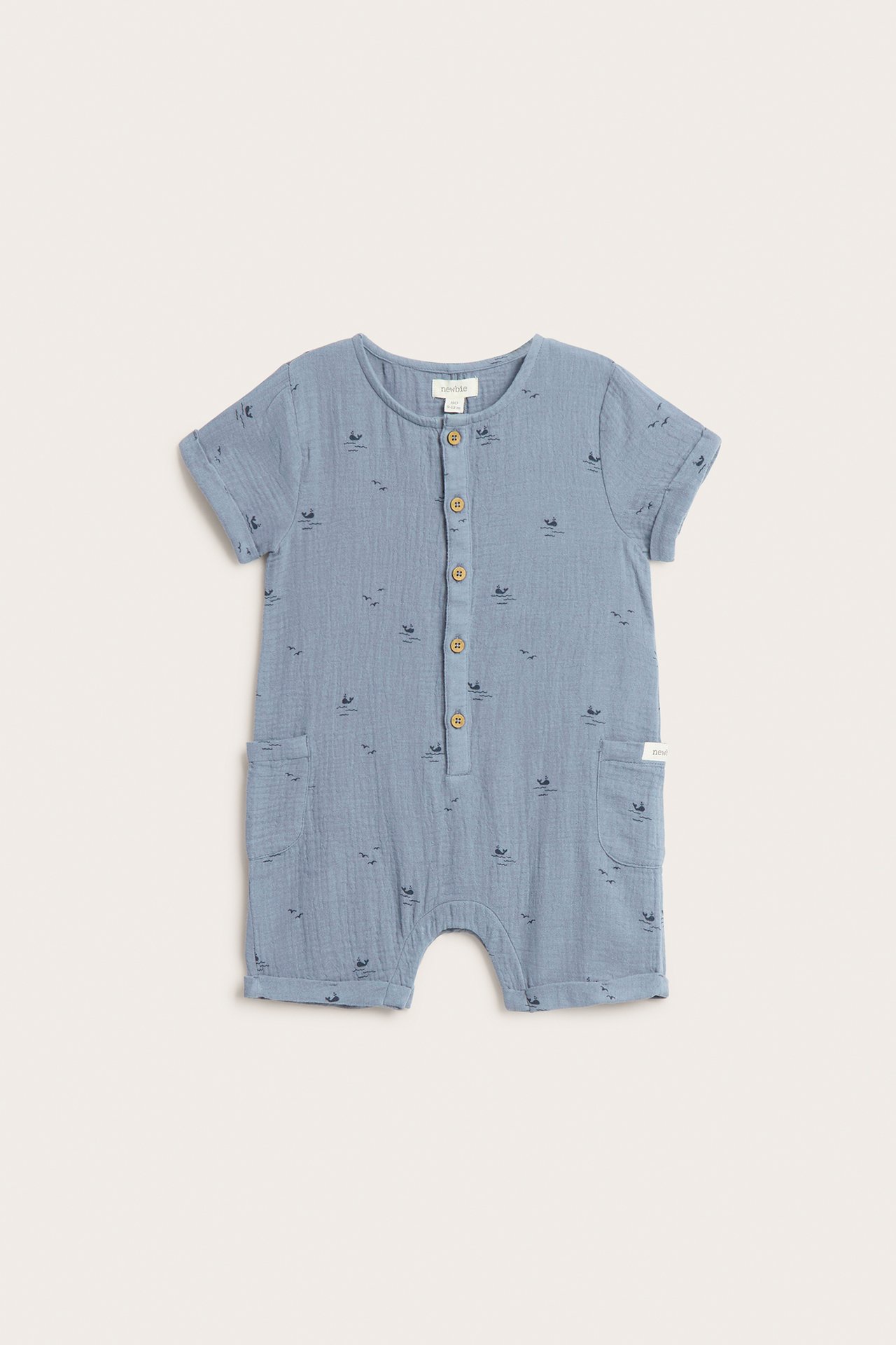 Front view: Baby's blue woven cotton short-sleeved romper with whale pattern, front buttons, and patch pockets.