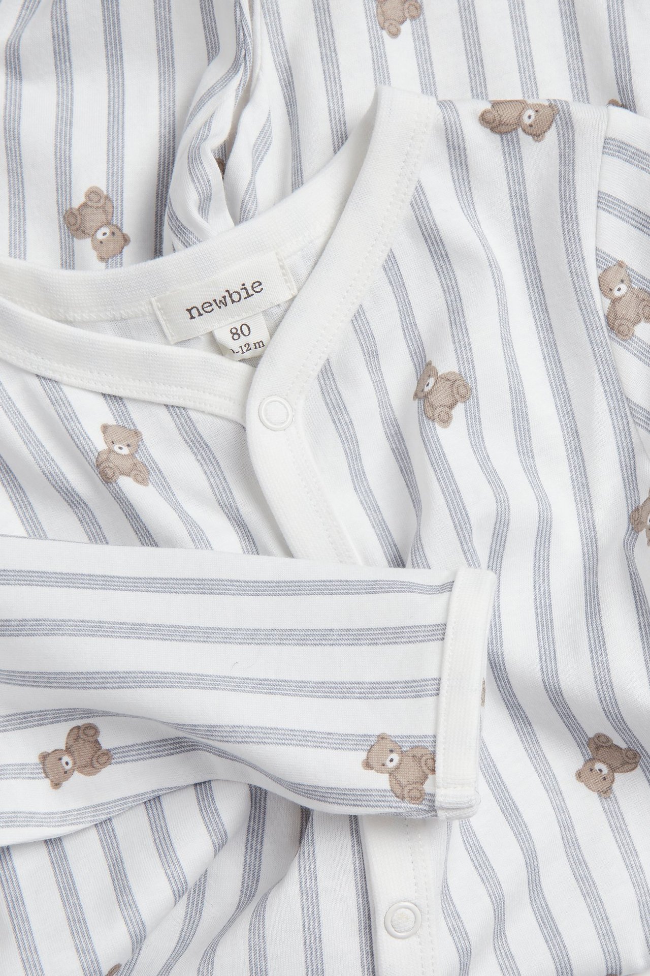 Nahaufnahme eines cremeweißen Baby-Baumwollpyjamas mit grauen Streifen, Teddybären und Druckknöpfen vorne.