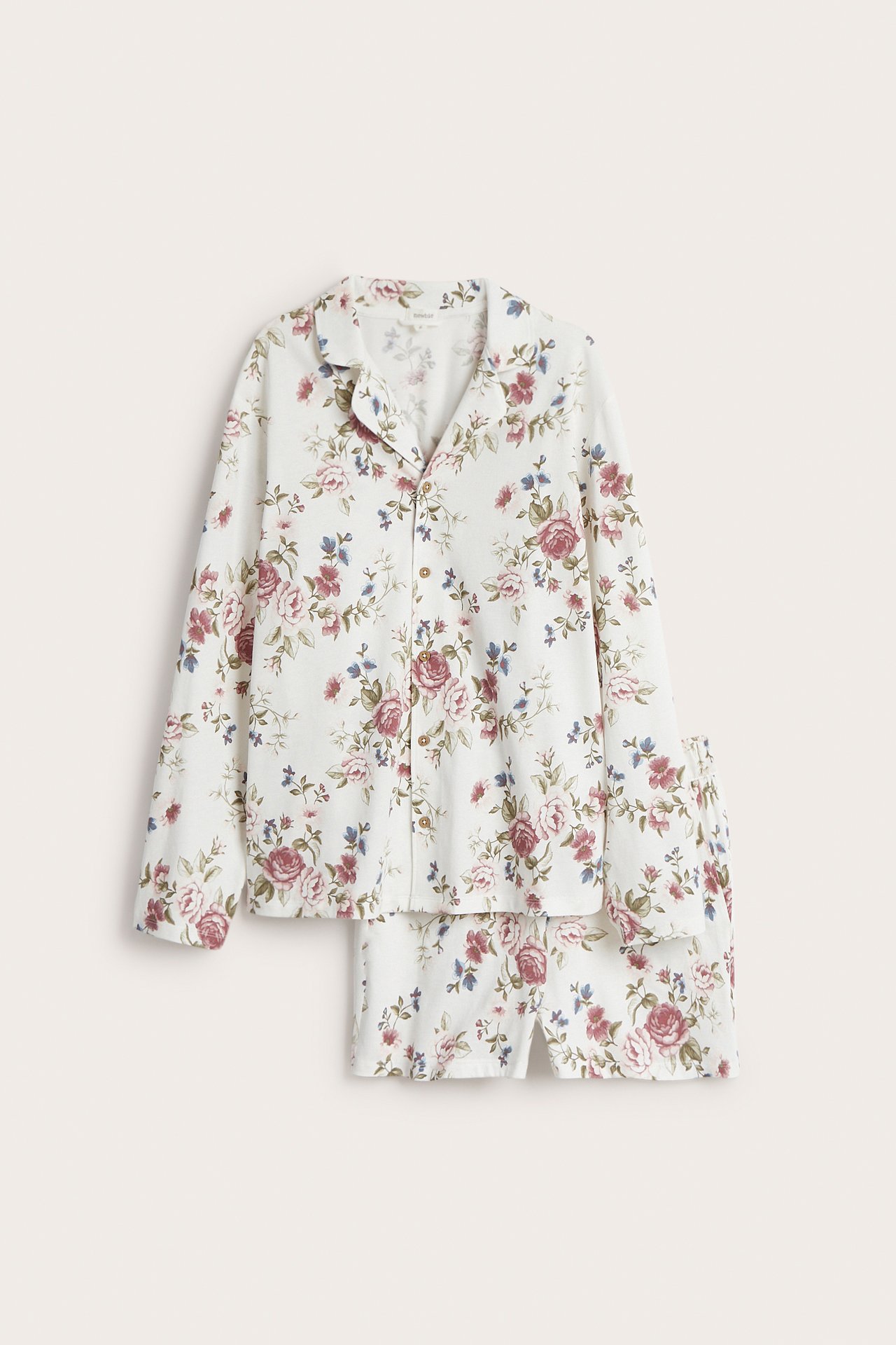 Front view of a white floral cotton pajama set with a long-sleeved button-up top and matching shorts.