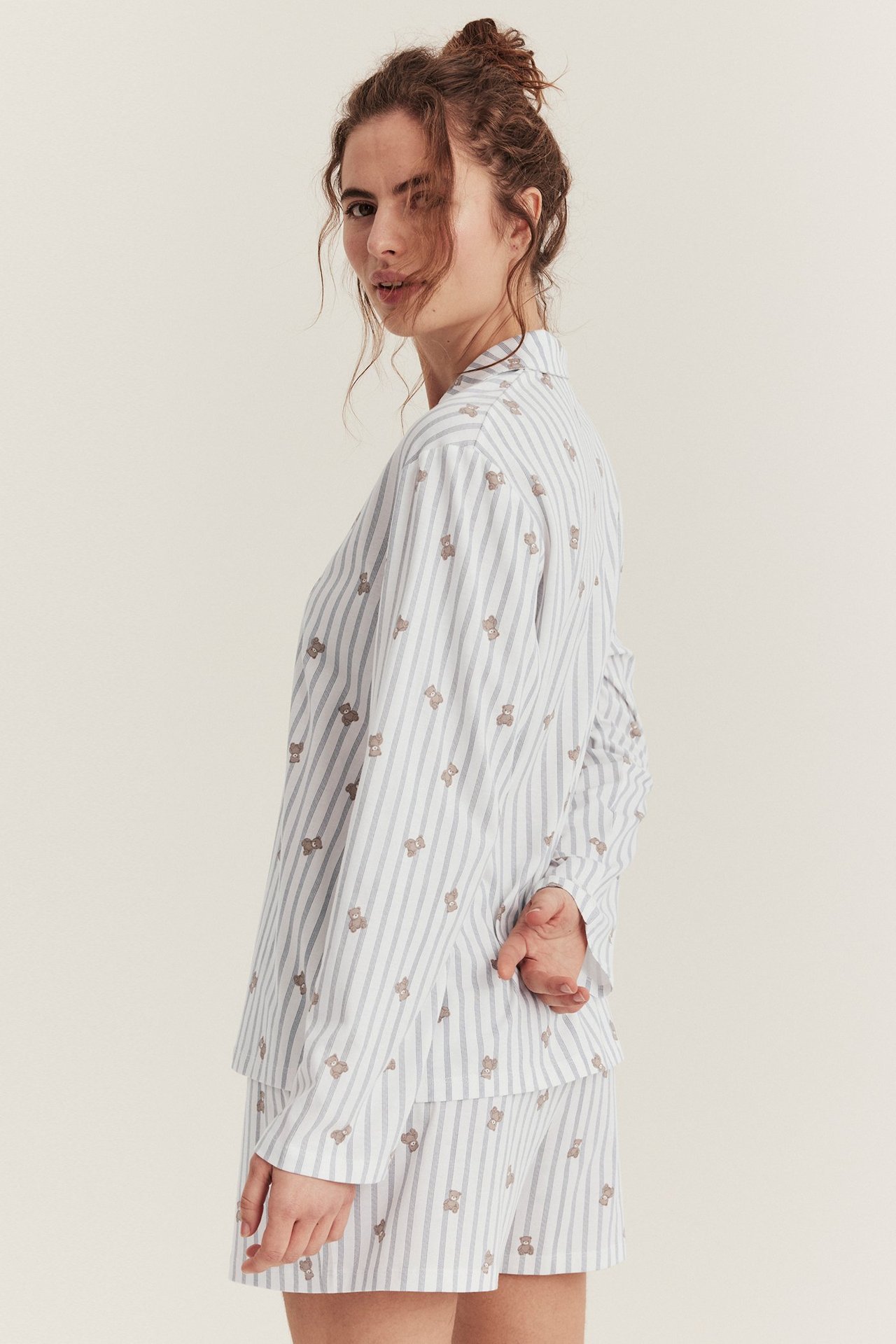 Seitenansicht einer Frau in einem cremefarbenen gestreiften Baumwoll-Pyjama-Set mit Teddybärmuster.