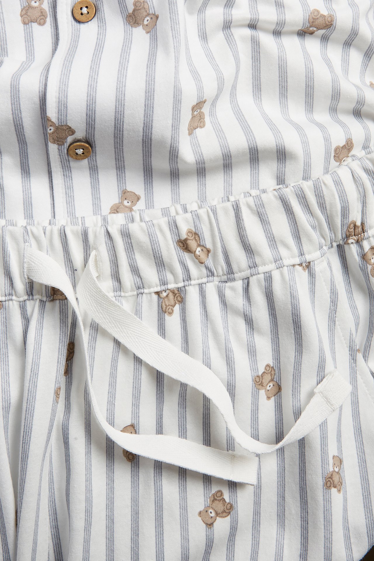 Nahaufnahme von cremeweißem Baumwolljersey-Pyjamaoberteil mit Knöpfen und Shorts mit Kordelzug, mit Bären- und Streifenmuster.