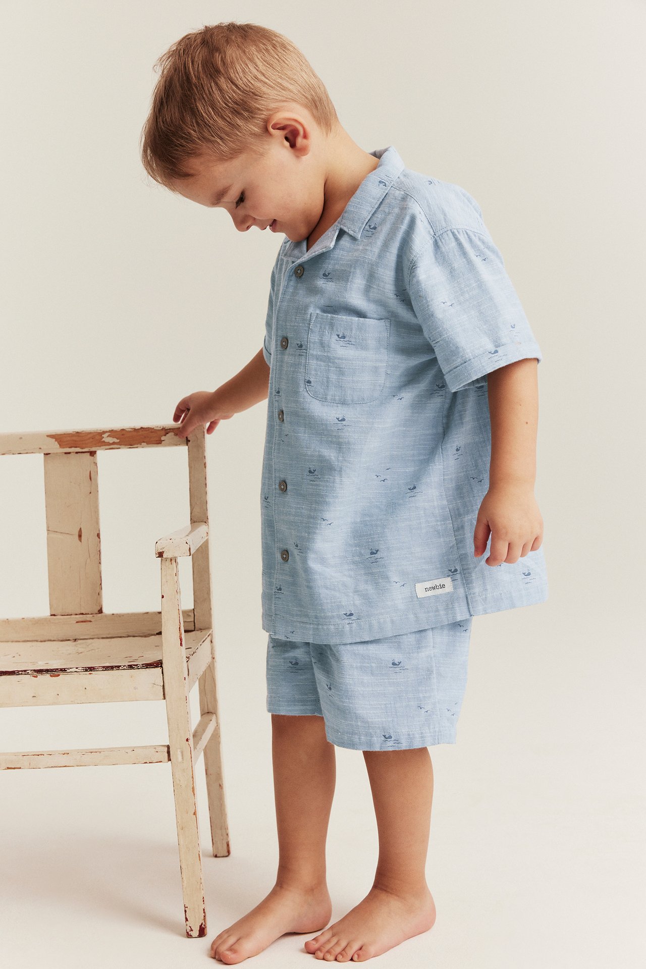 Seitenansicht eines Kindes in hellblauen Chambray-Shorts mit Walmuster und passendem kurzärmeligem Hemd.