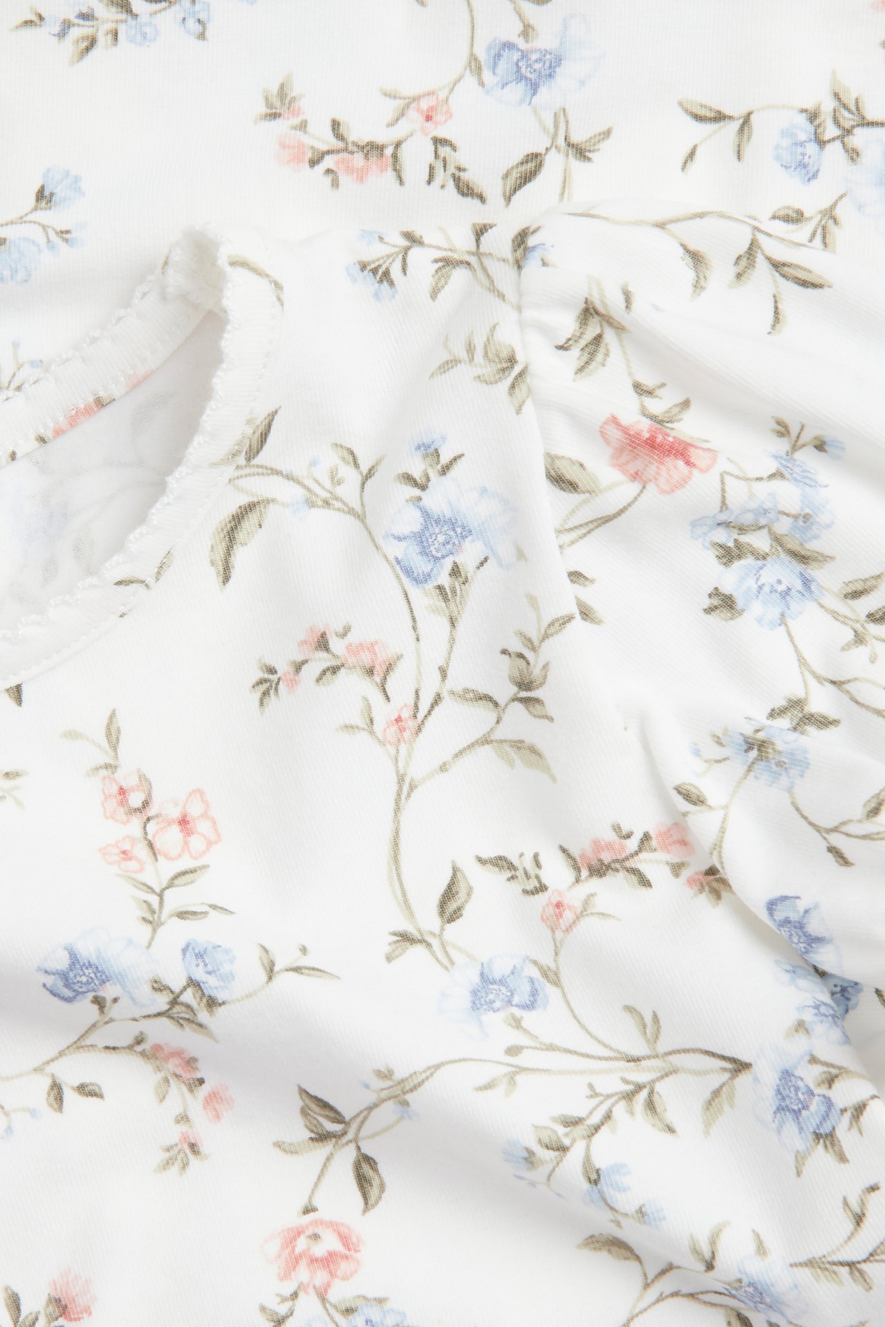 Close-up of an off-white short-sleeved floral top with blue/pink flowers, puff sleeves, and picot trim.