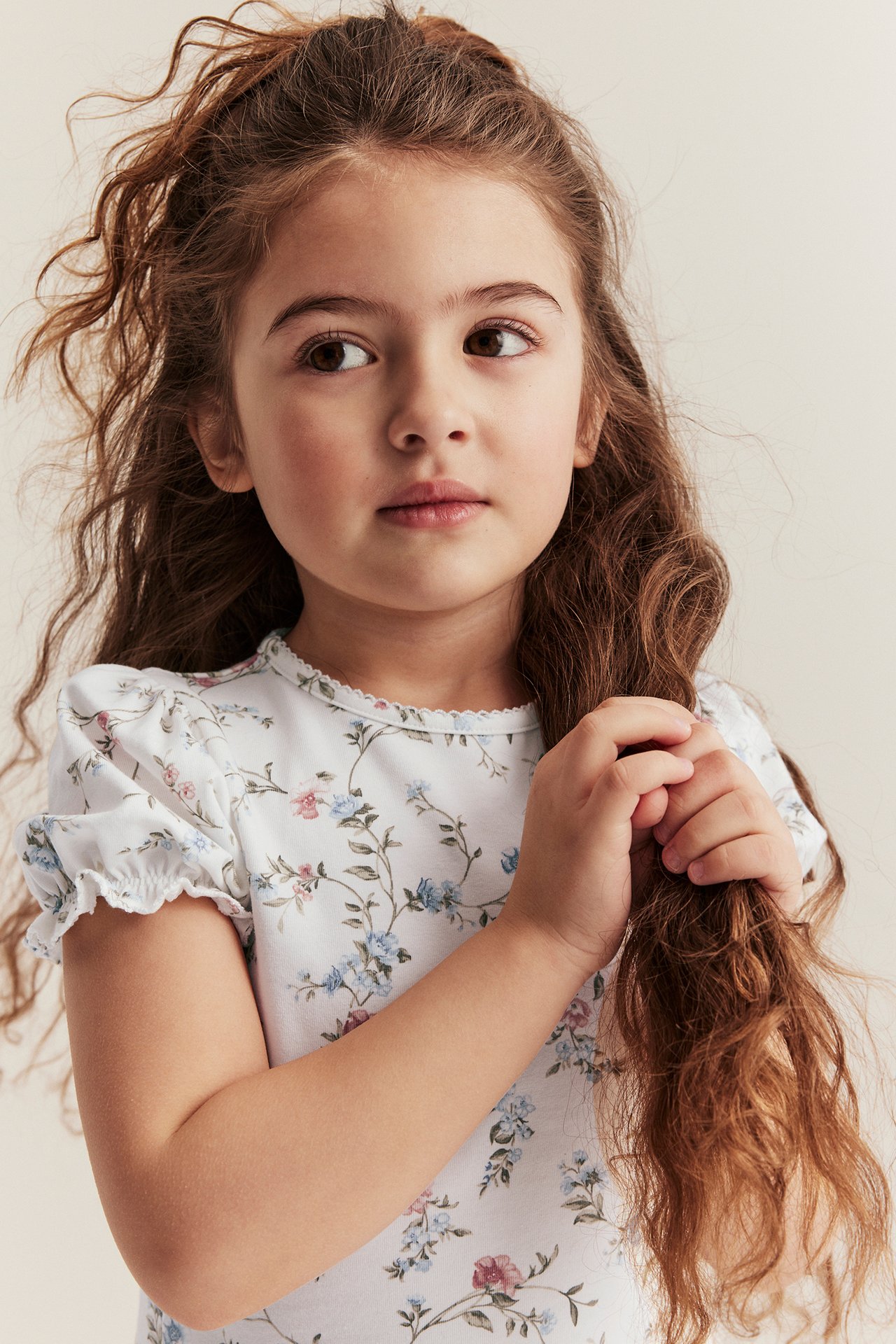 Close-up of a kid in an off-white floral short-sleeved top with puff sleeves, holding her hair.
