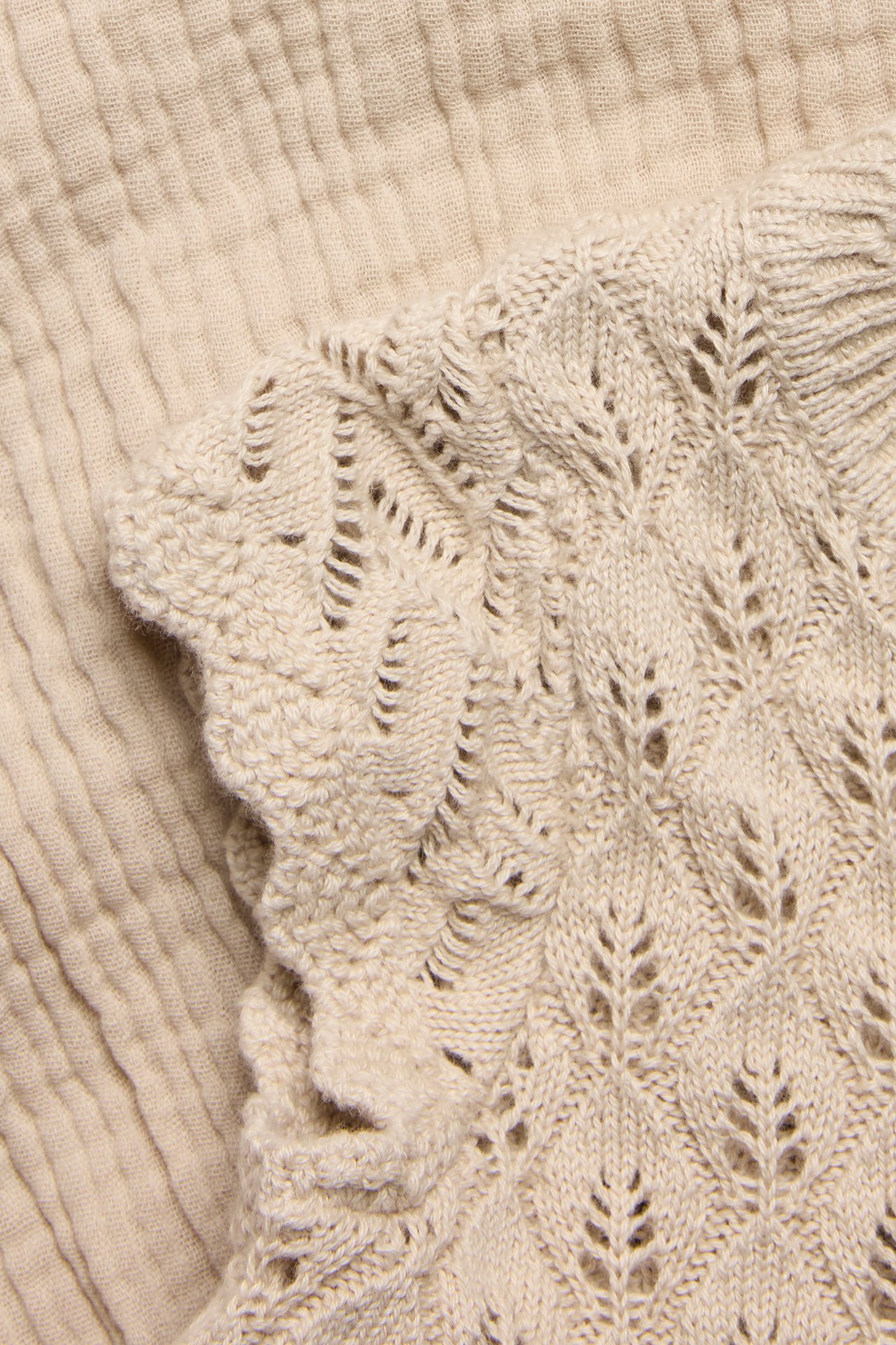 Nahaufnahme eines beigen Strickkleides mit Spitzenmuster, Wellenkante und gewebtem Musselin-Unterteil.
