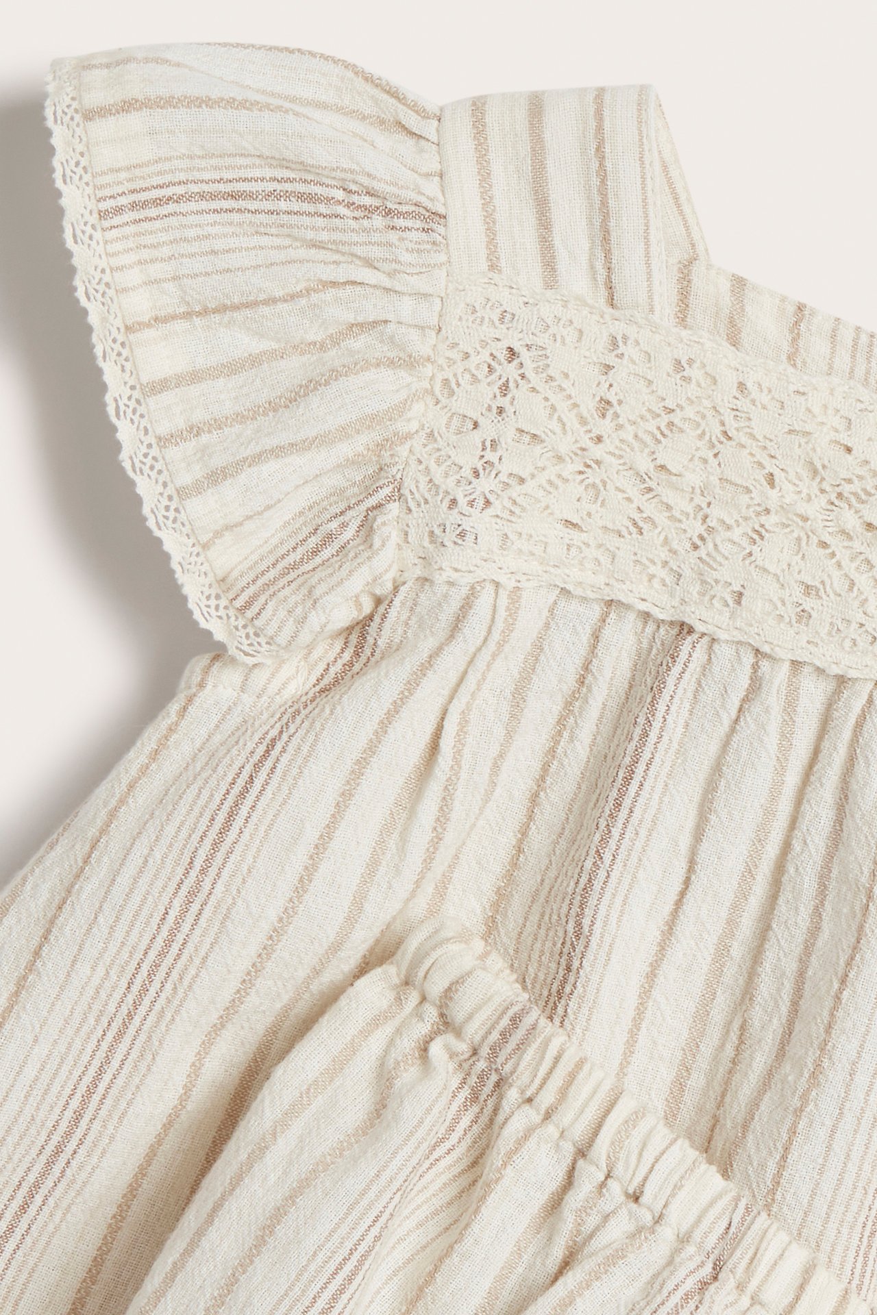 Nahaufnahme eines gestreiften Offwhite-Sets für Kinder: Bluse mit Spitzenbesatz, Rüschenärmeln und elastischen Shorts.