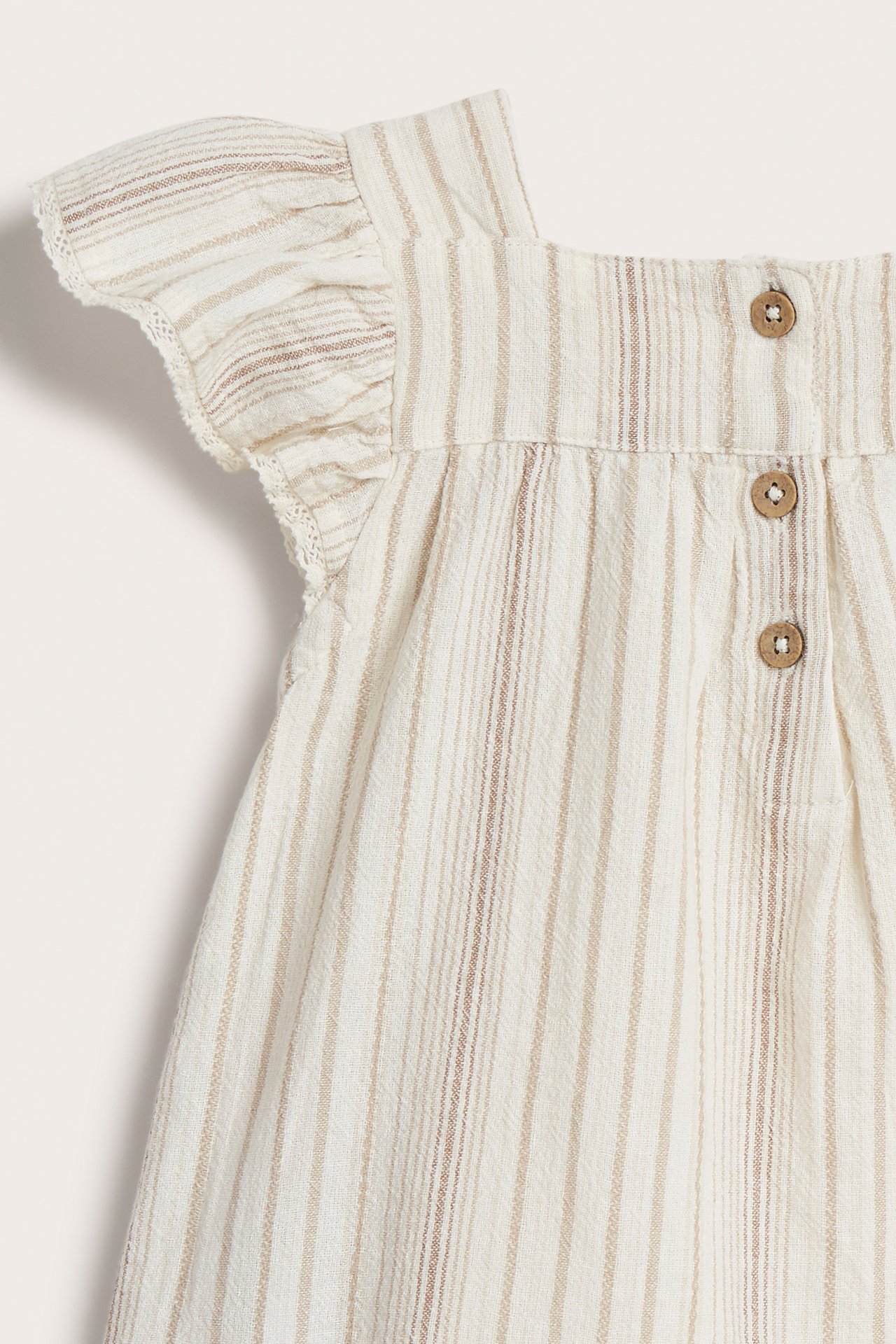 Nahaufnahme Rückansicht einer gestreiften off-white gewebten Kinderbluse mit Rüschenärmeln, Spitzenbesatz und Holzknöpfen.