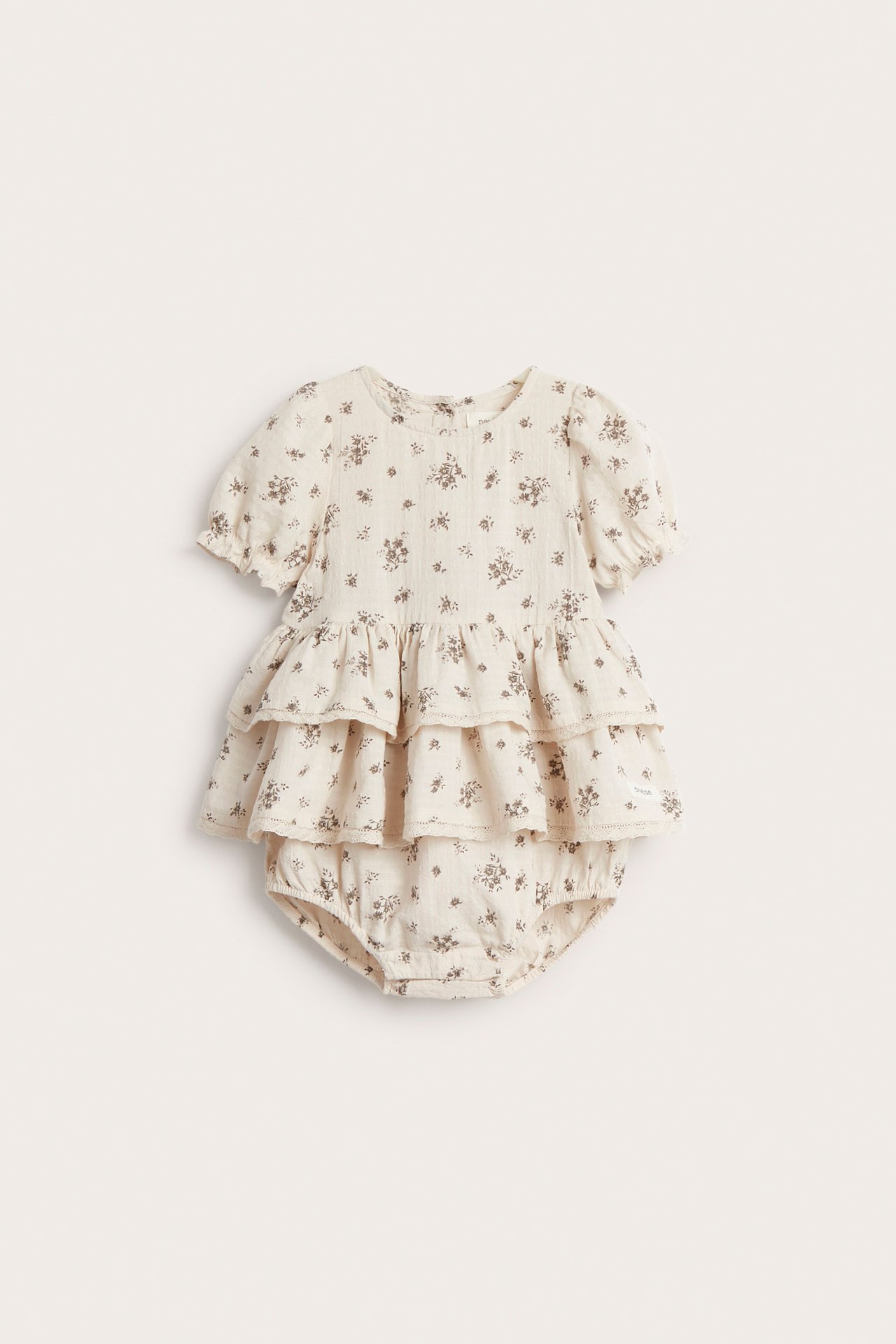 Front view of a baby's light beige floral cotton playsuit with ruffled tiers and short elasticated sleeves.