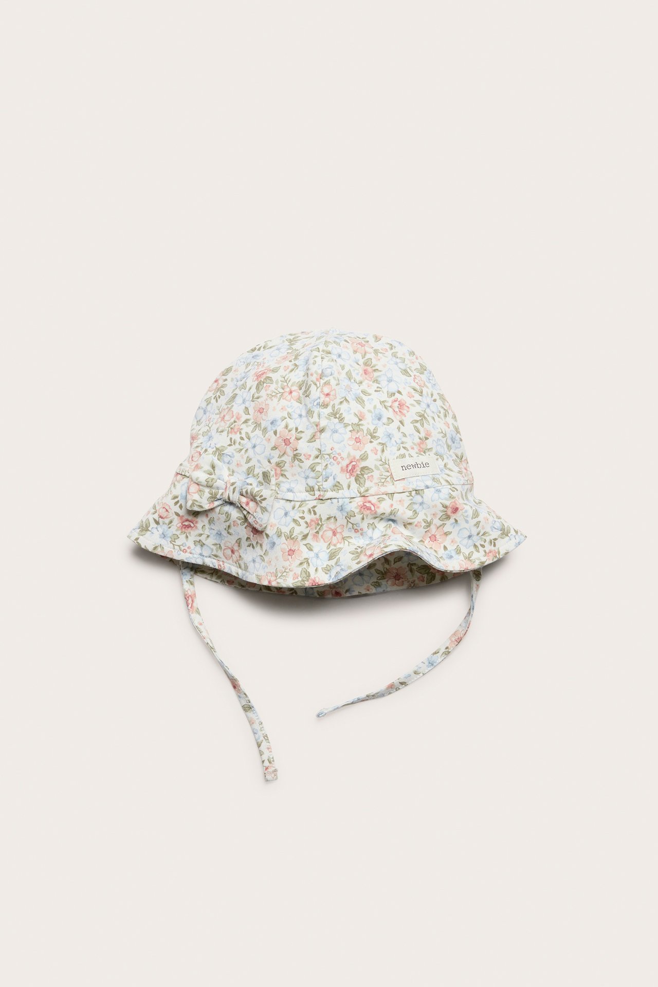 Vorderansicht eines cremefarbenen Baby-Sonnenhuts mit Blumenmuster, Schleife vorne und Bindebändern.