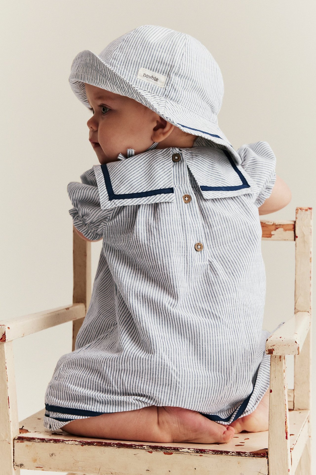 Rückenansicht eines Babys in gestreiftem Baumwollkleid mit marineblauem Matrosenkragen und passendem Hut.