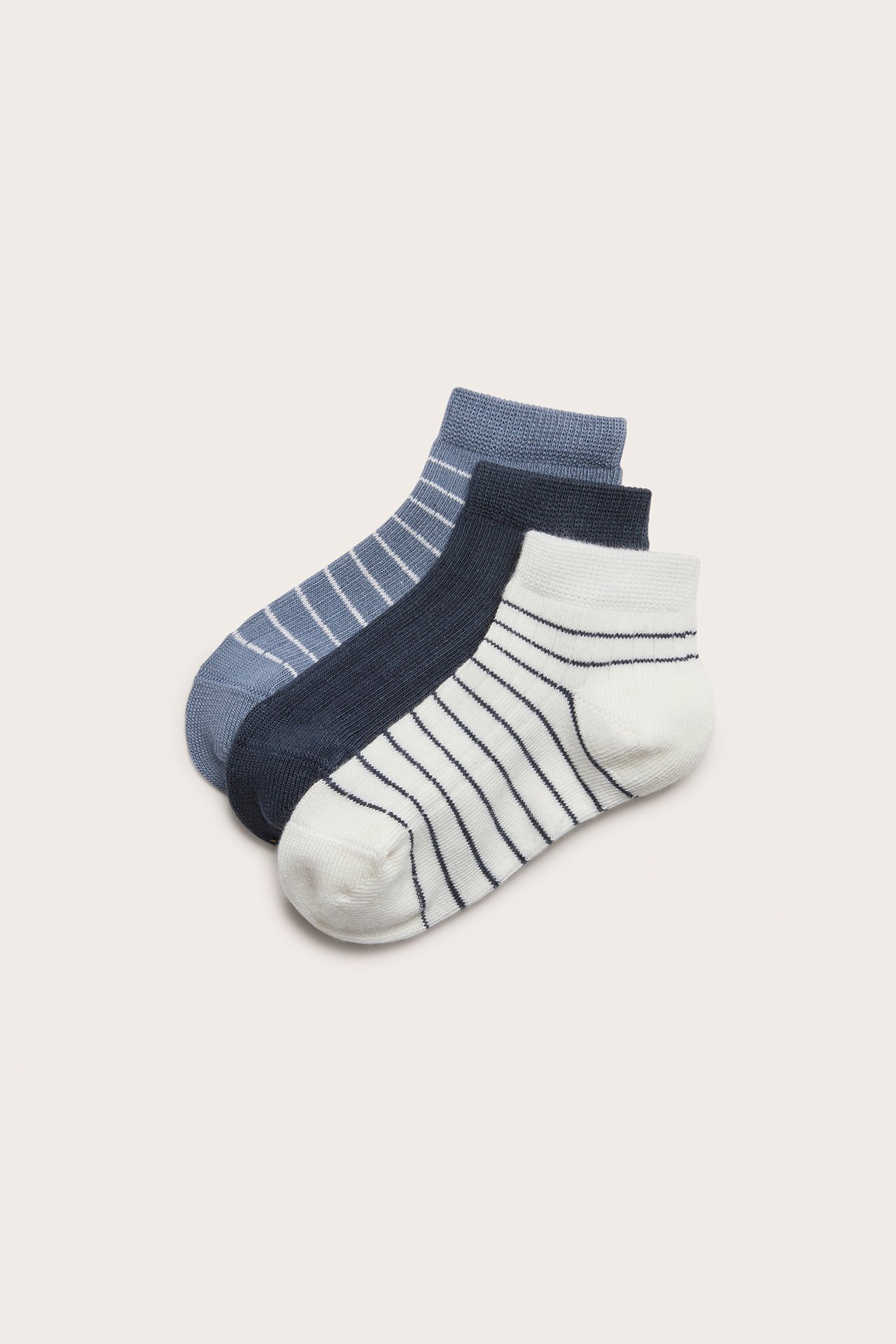 Top-down view of a 3-pack of ribbed ankle socks: one off-white striped, one dark blue, and one light blue striped.