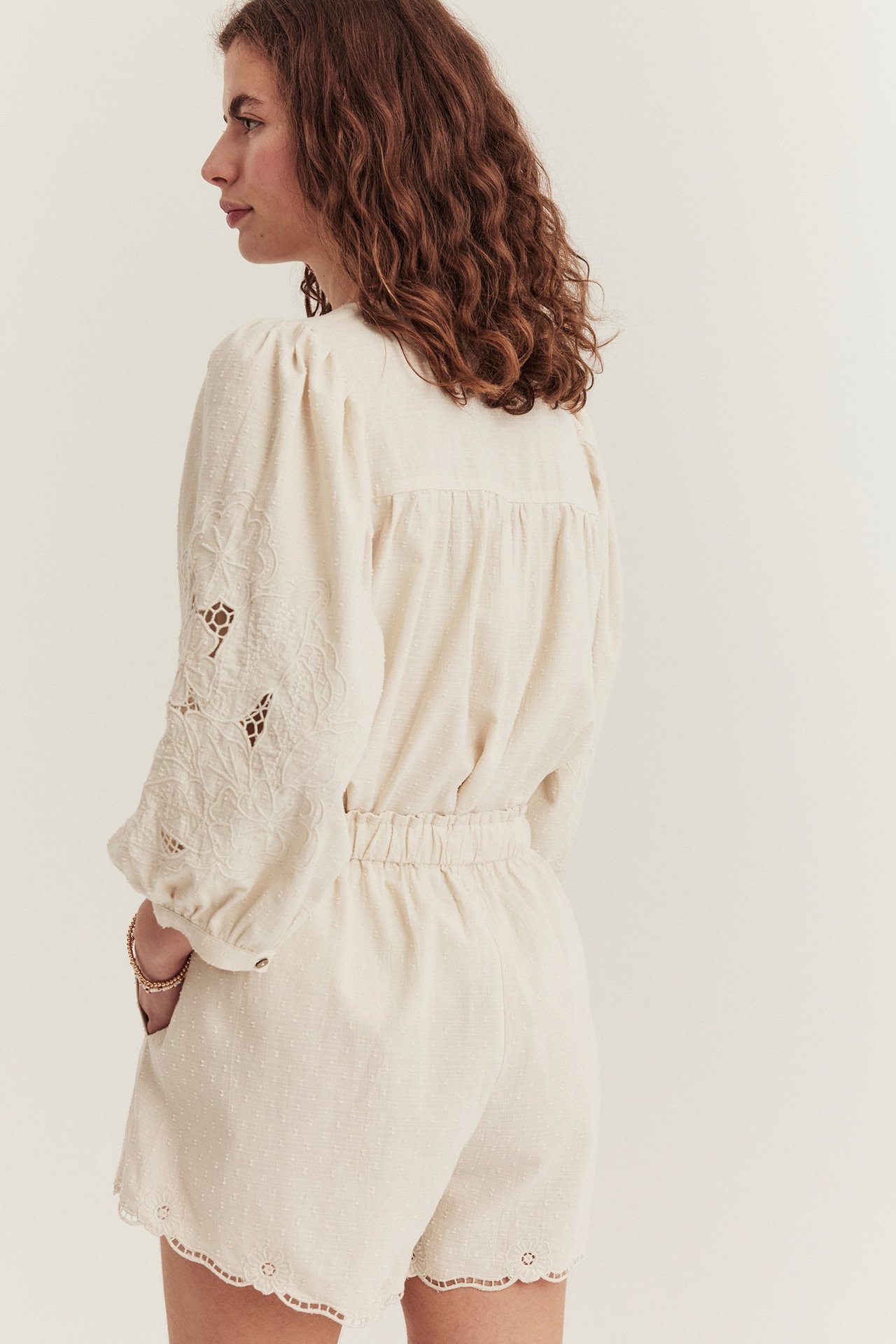 Seitenansicht einer Frau in hellbeigen gewebten Shorts mit besticktem Saum und passender Bluse.