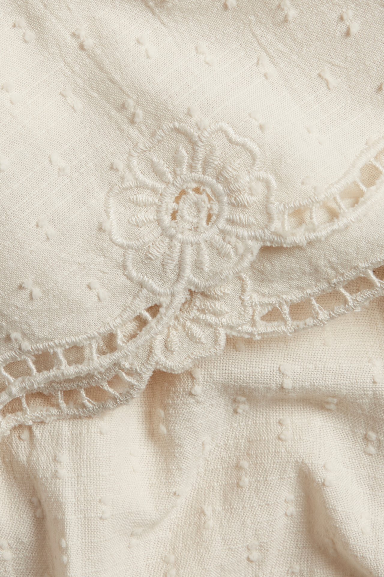Close-up of light beige woven shorts with dotted texture and intricate floral embroidery with cut-outs.