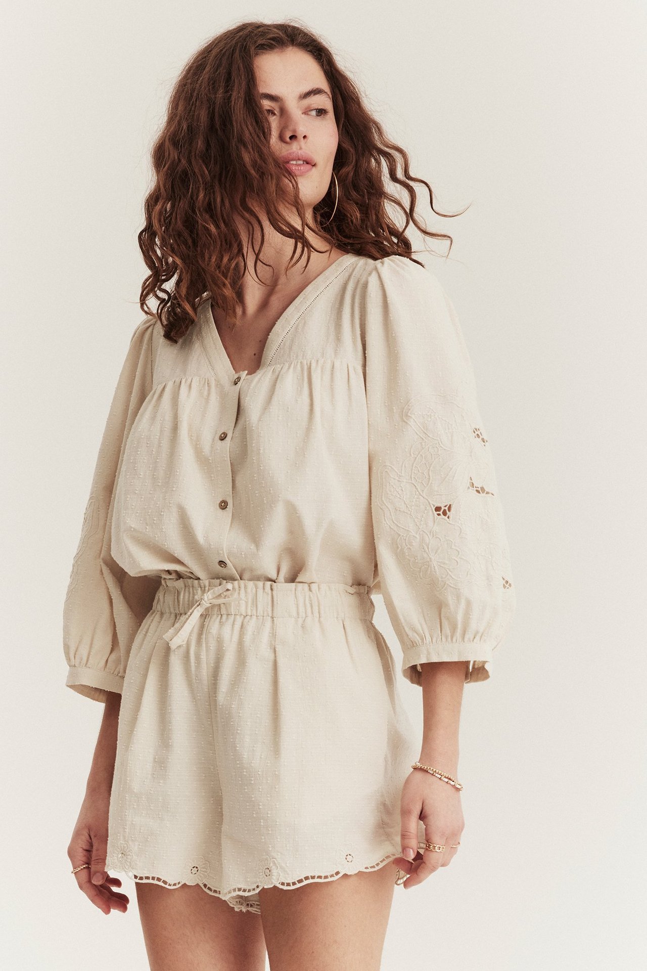 Vorderansicht einer Frau in hellbeigen gewebten Shorts mit bestickten Wellensäumen und passender Bluse.