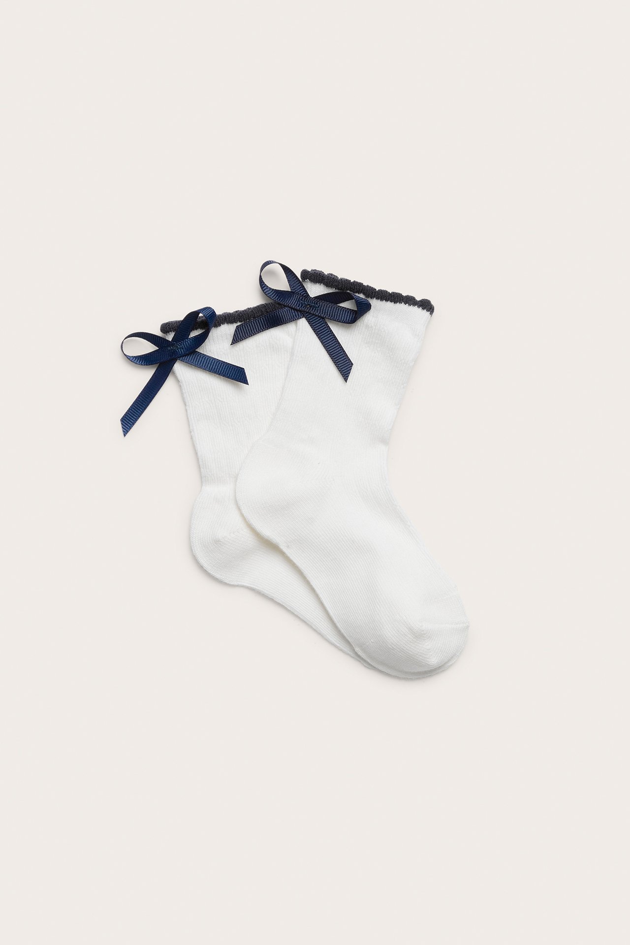 Draufsicht auf ein Paar cremeweiße Socken mit dunkelblauen Schleifen und dunklem Wellenrand.