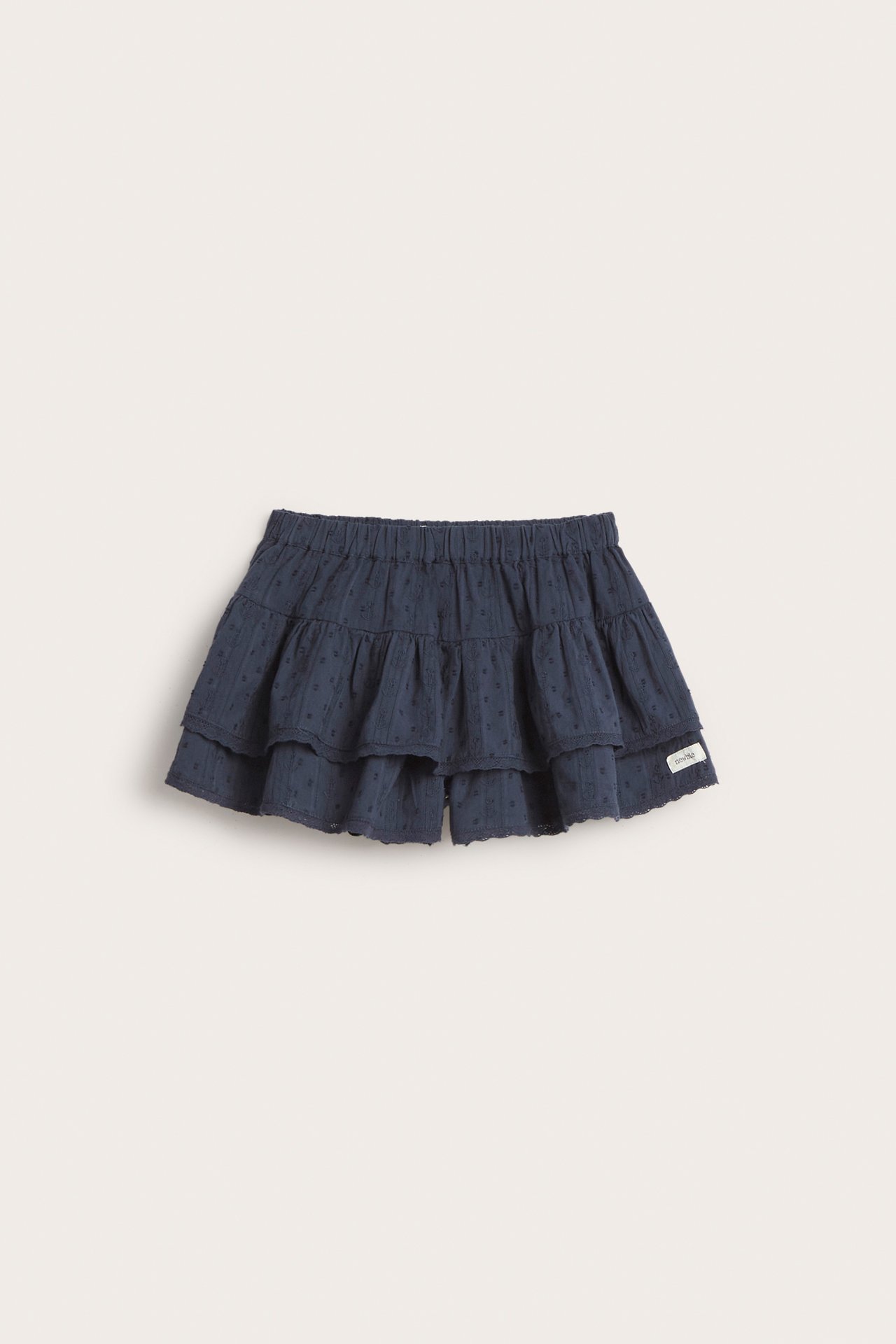 Front view of a kid's dark blue woven cotton shorts-skirt with two ruffled tiers and a dobby dot pattern.