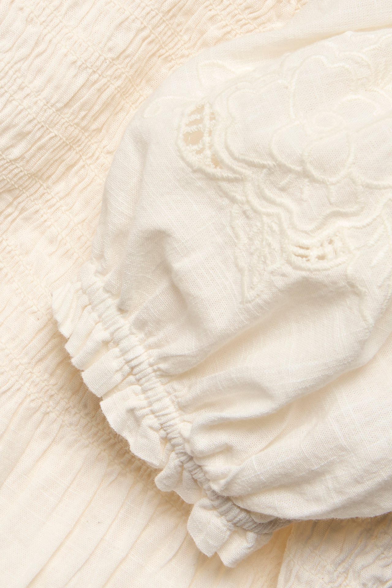 Close-up of an off-white cotton blouse with smock detailing, embroidered puff sleeve, and elasticated cuff.