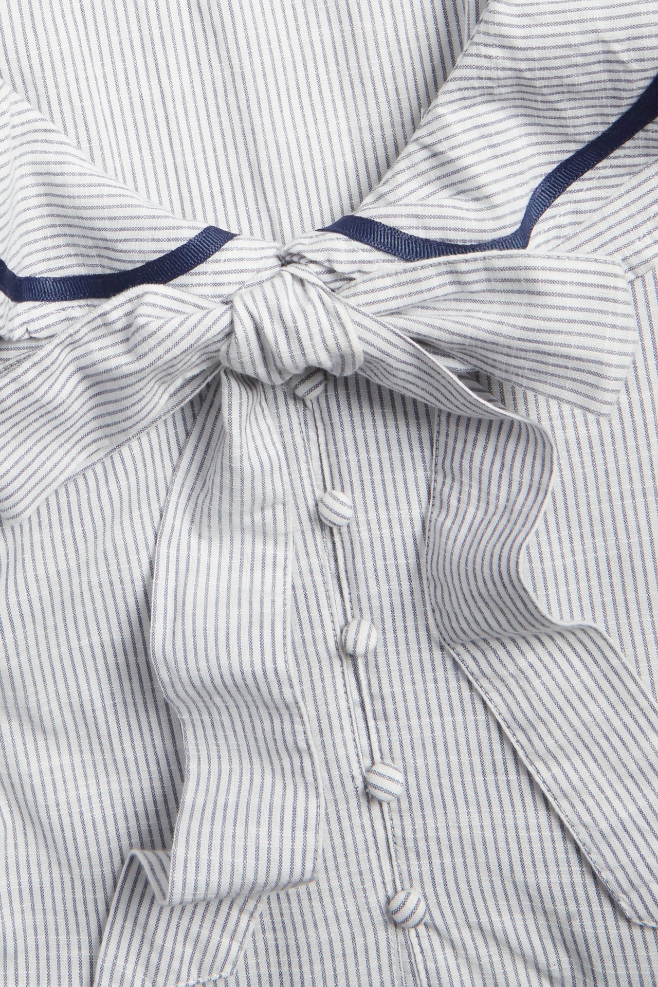 Nahaufnahme: Off-weißes gestreiftes Baumwollkleid mit Rüschenkragen, blauem Band, Schleife vorne und bezogenen Knöpfen.