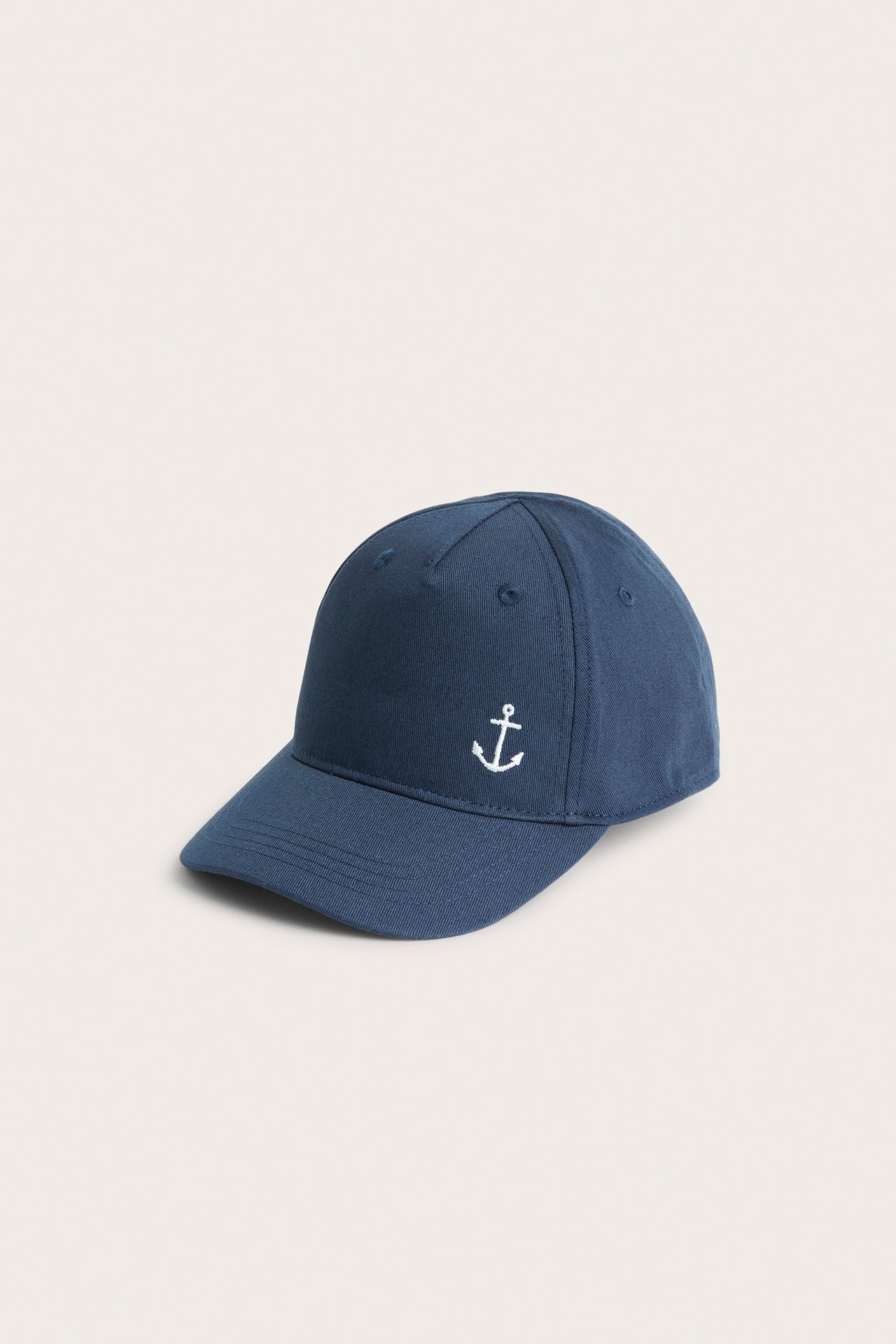 Front-side view of a kid's dark blue solid baseball cap with a small white anchor embroidery.