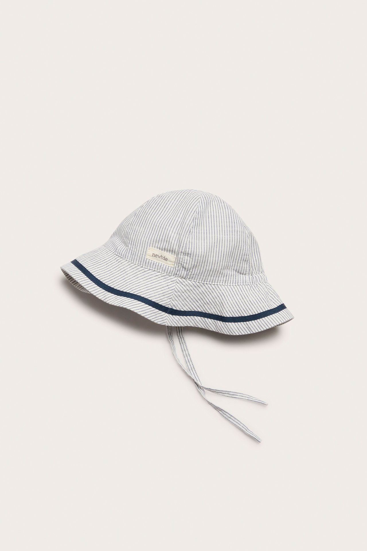 Side view of an off-white striped baby sun hat with a blue ribbon on the brim and tie straps.