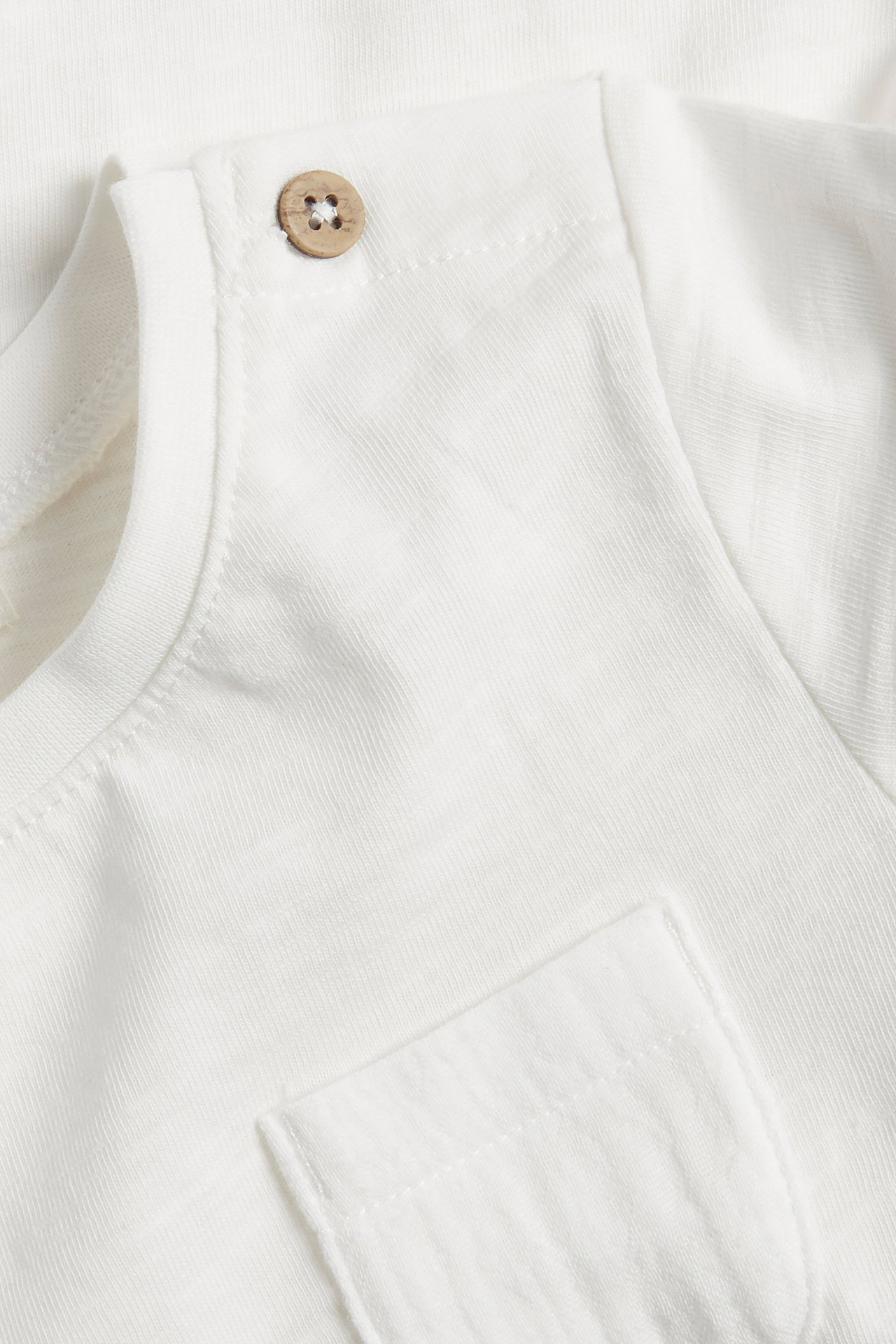 Close-up of an off-white baby's short-sleeved cotton bodysuit with a wooden shoulder button and chest pocket.