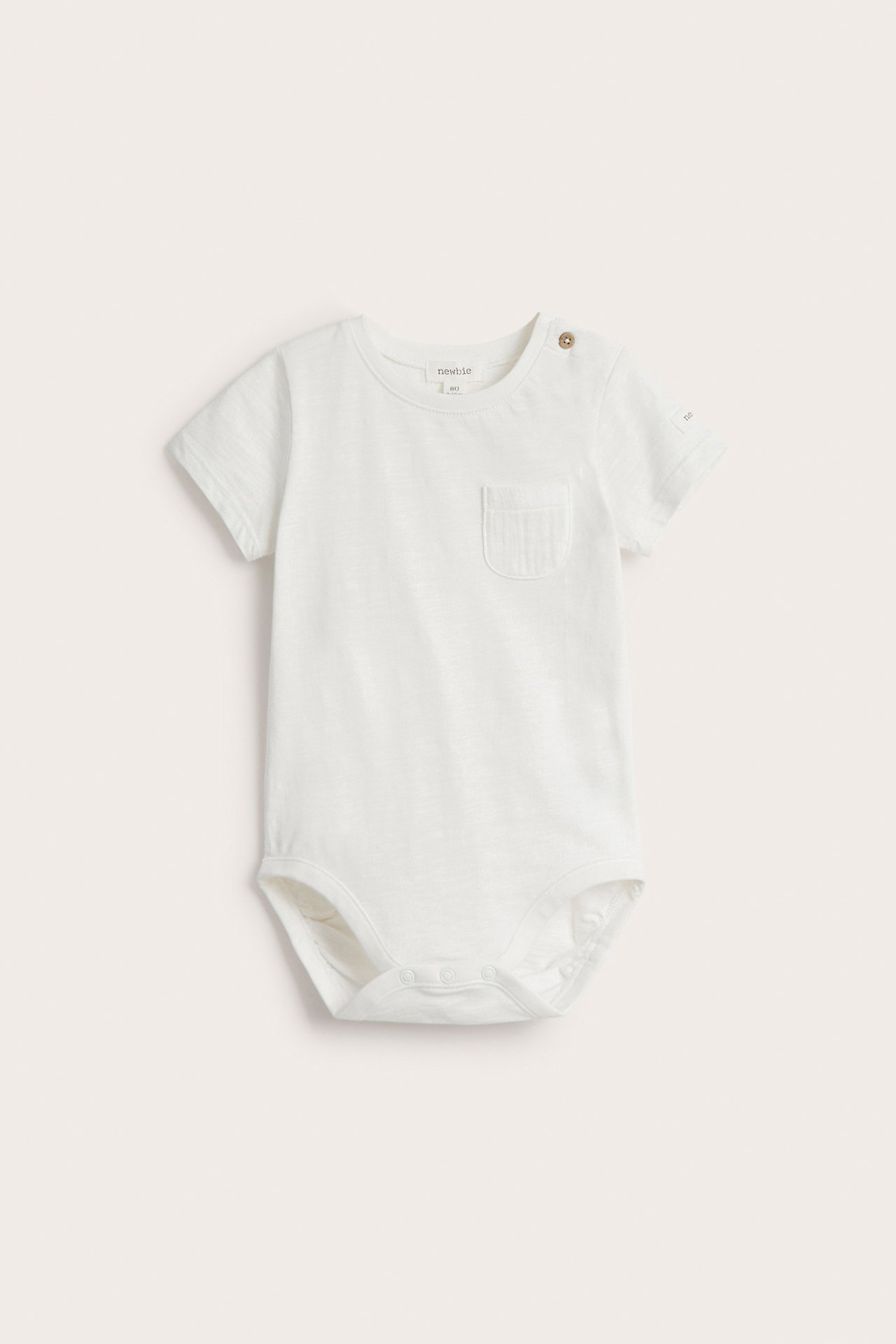 Front view: Off-white short-sleeved baby bodysuit with shoulder and crotch snaps, plus a chest pocket.