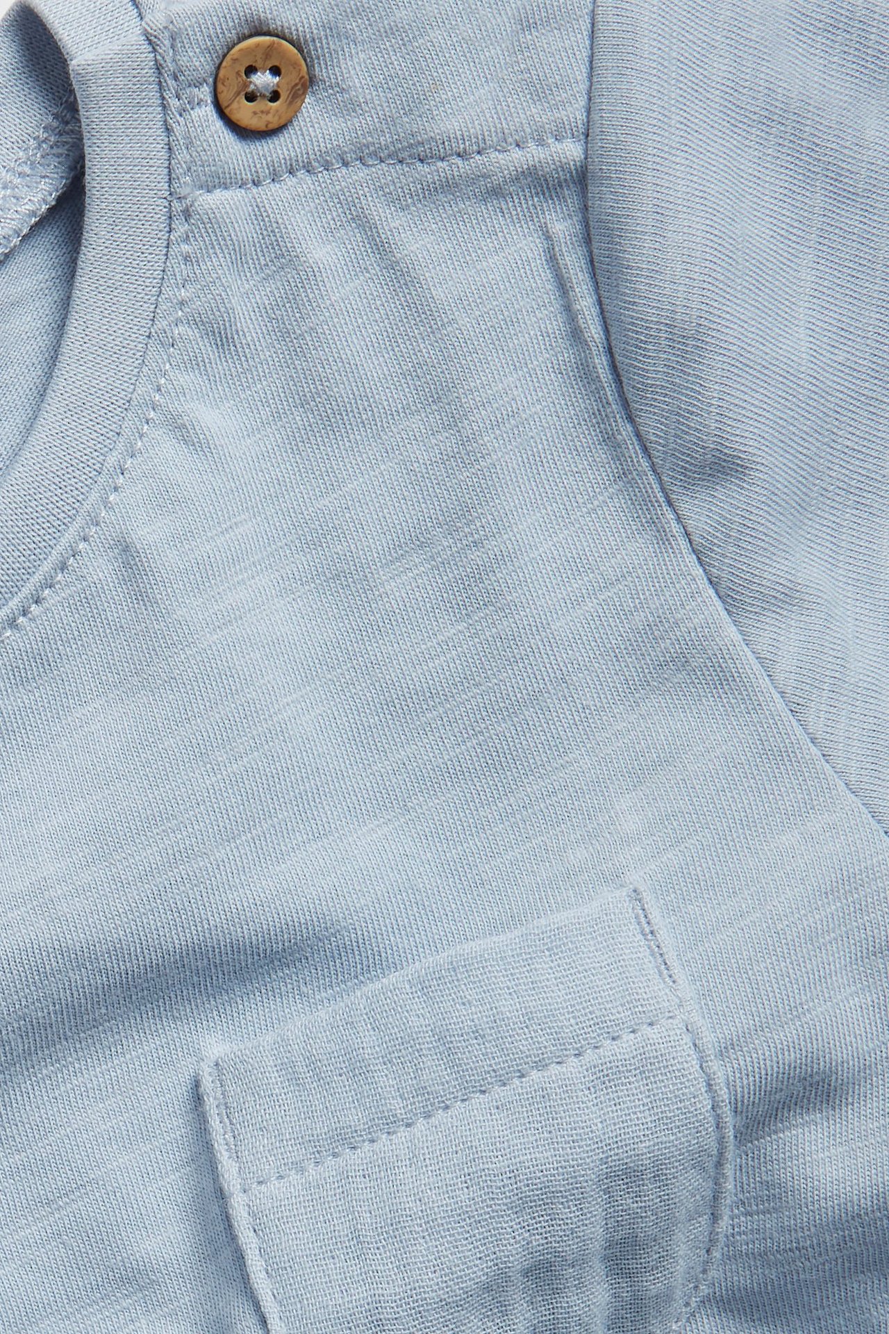 Close-up of a light blue baby bodysuit in slub jersey with a wooden shoulder button and chest pocket.