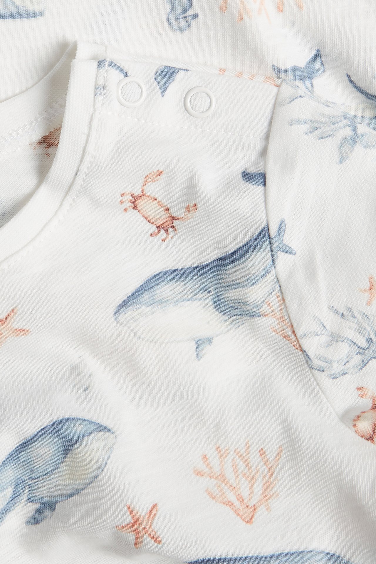 Close-up of an off-white short-sleeved baby bodysuit in slub jersey with a sea animal pattern and shoulder snap buttons.